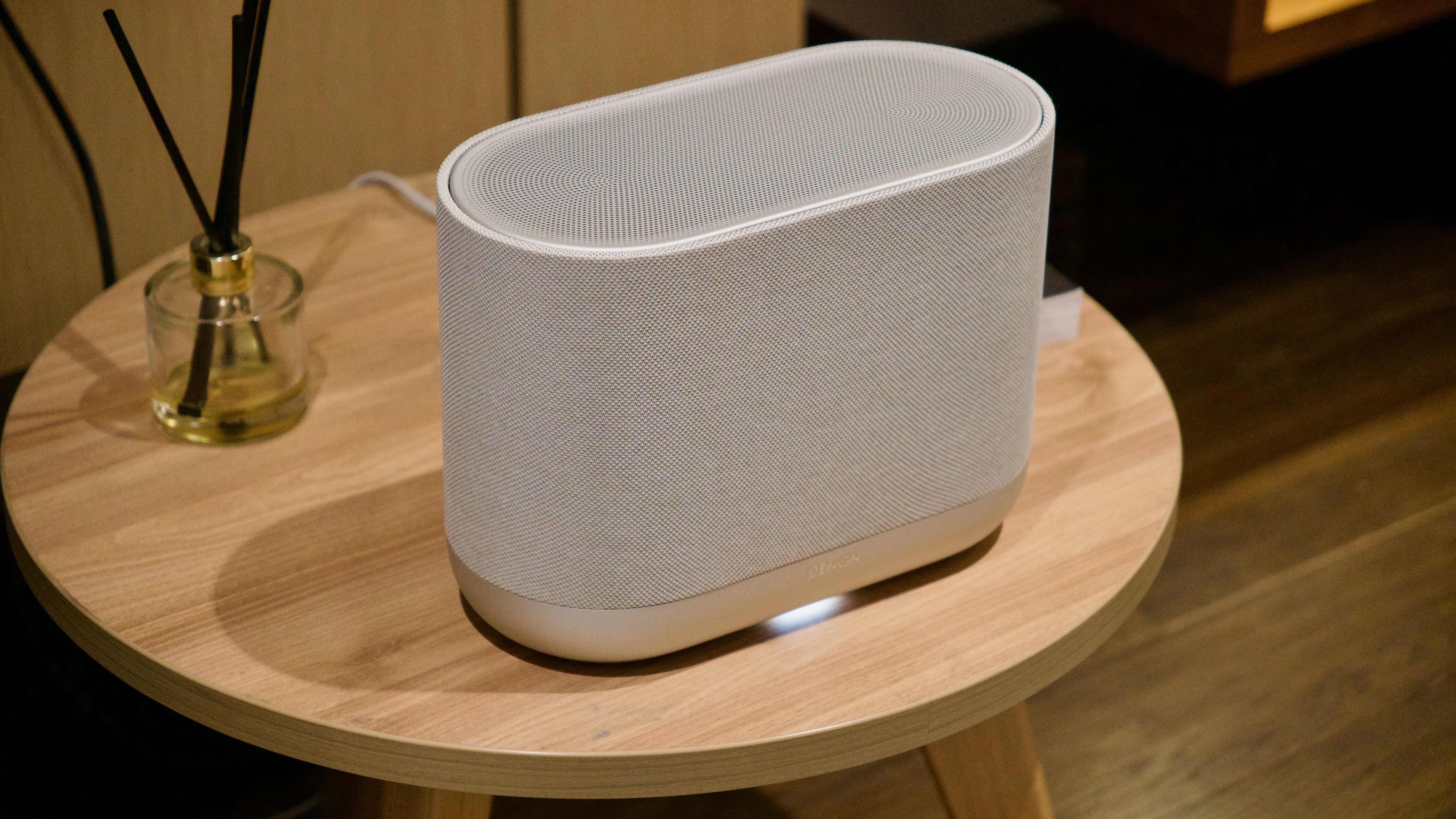 Denon Home 400 home speaker on a wooden surface, next to a diffuser