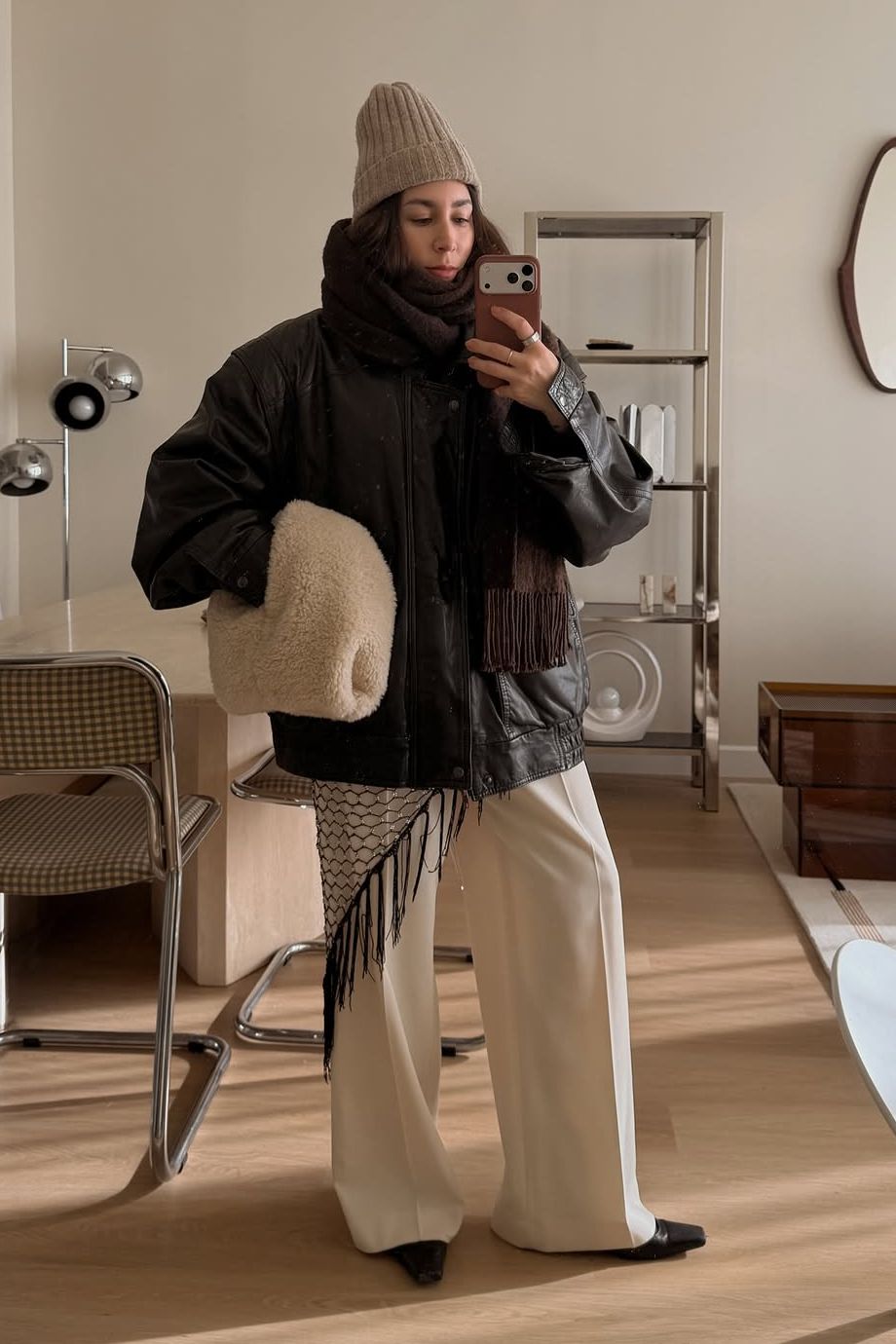 Lauren Caruso posing in mirror wearing beanie, scarf, leather jacket, and beige pants