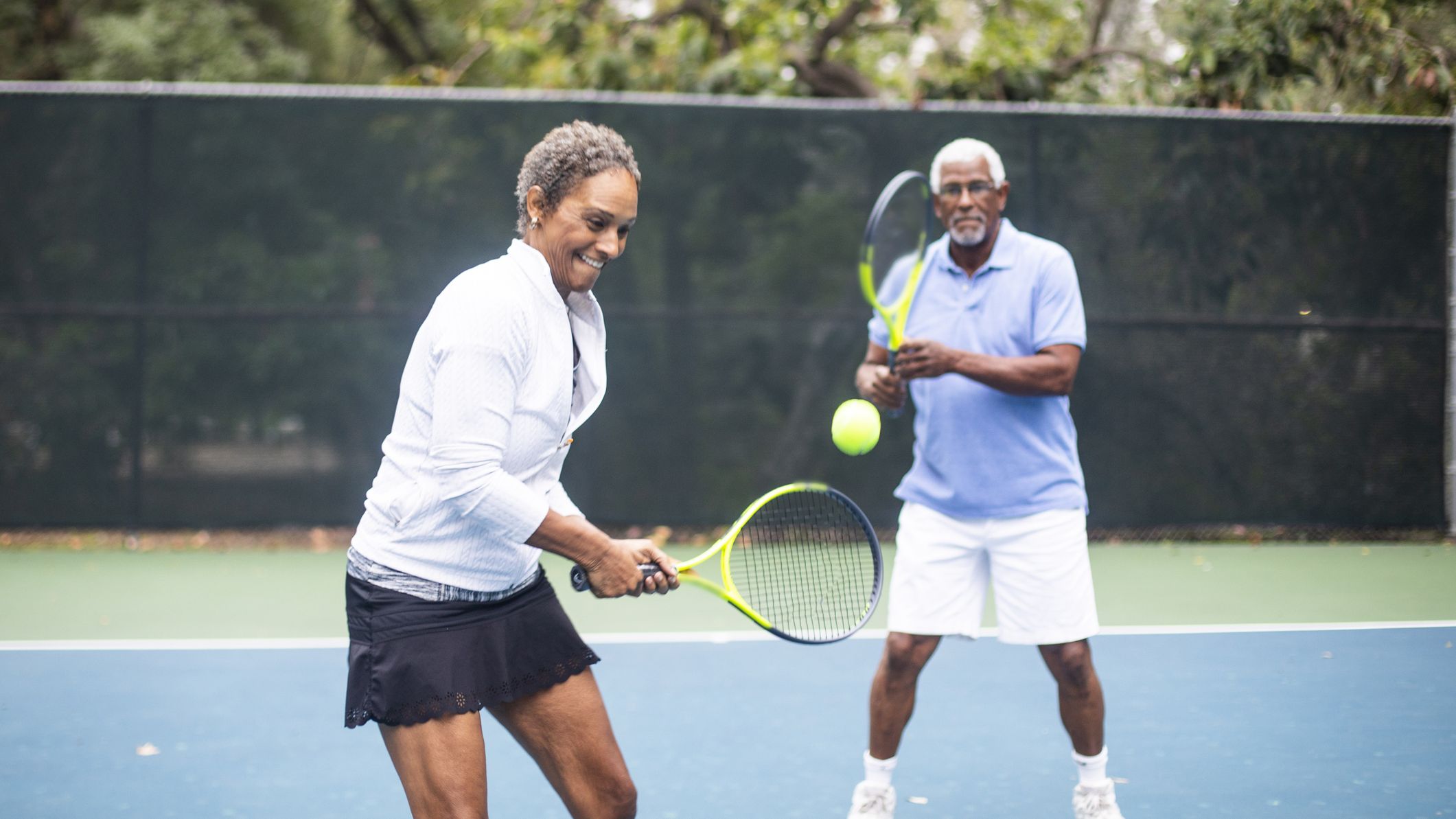A senior black couple playing doubles tennis on a cloudy morning.