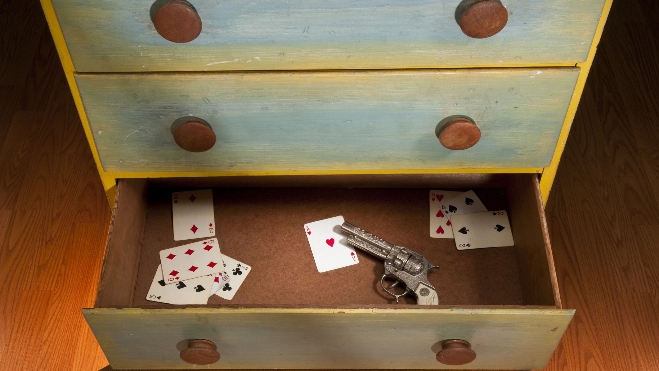 An open drawer contains a few playing cards and a pistol or hand gun.
