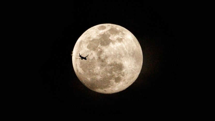 A full moon is photographed flying across a full moon in a black sky.