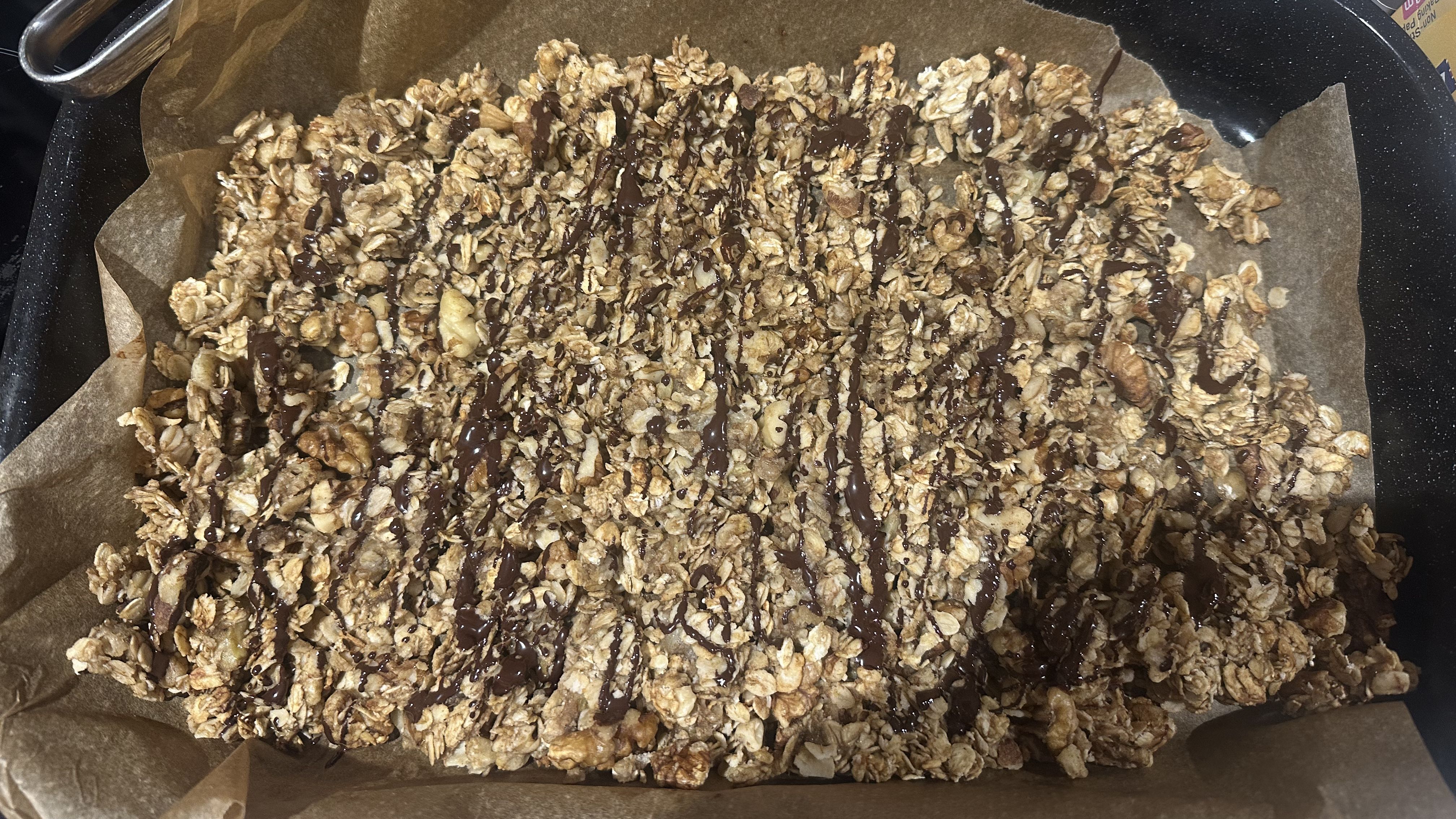 Granola in baking pan lined with baking paper drizzled with melted chocolate