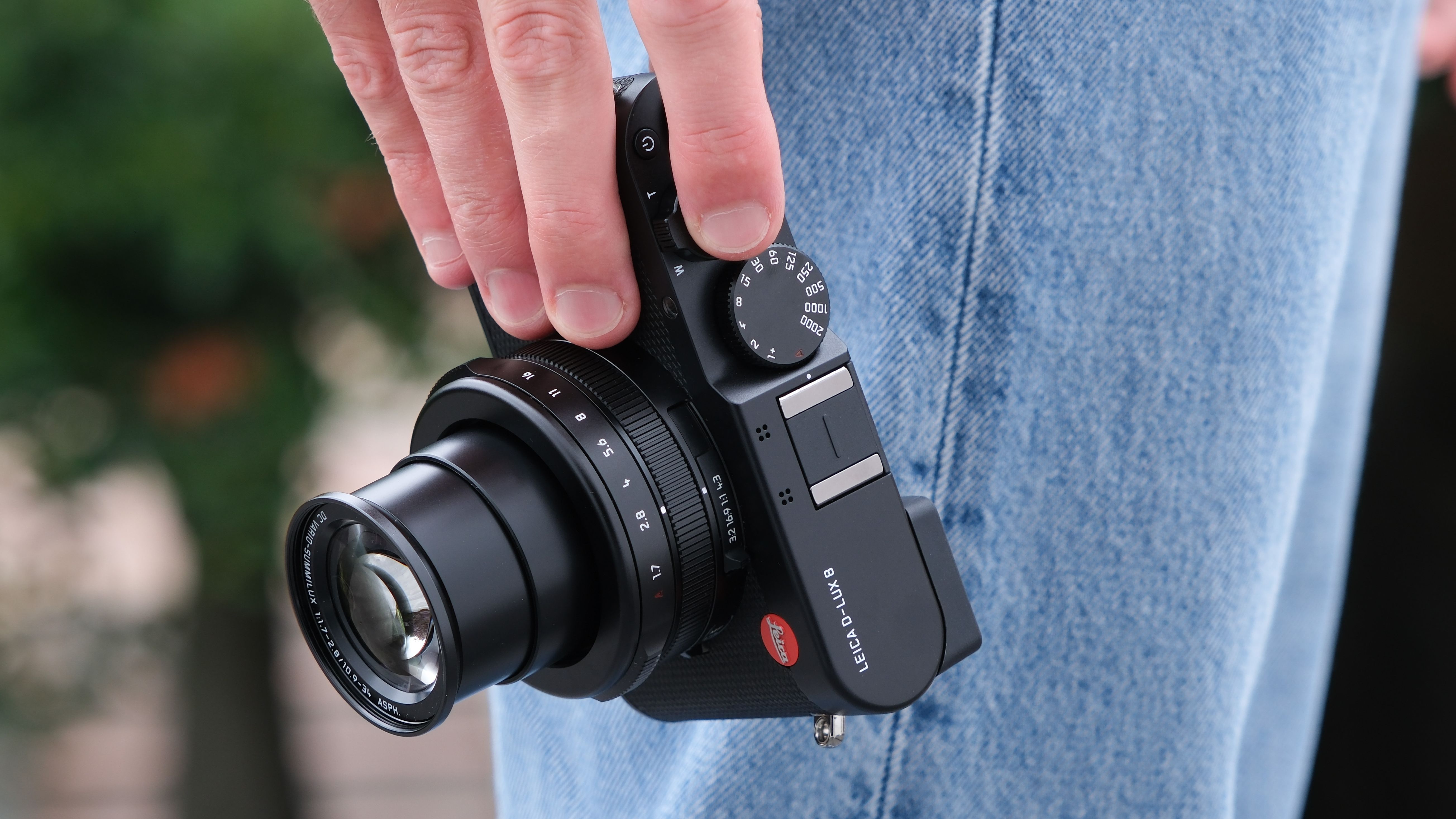 Leica D-Lux 8 camera held in a hands next to a persons side