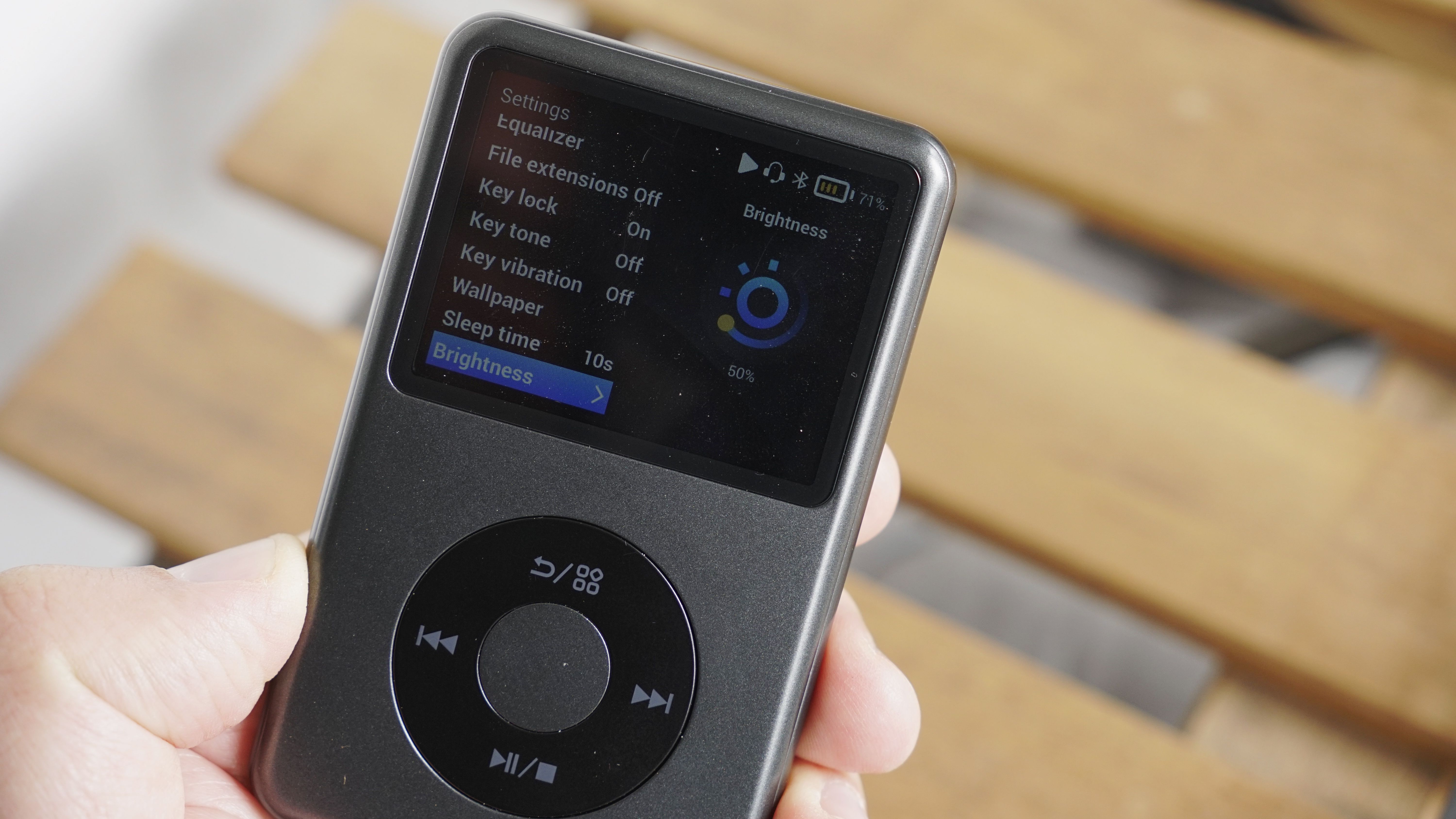 Innioasis Y1 player held in a man's hand, showing the dial and screen, with a wooden table in the background