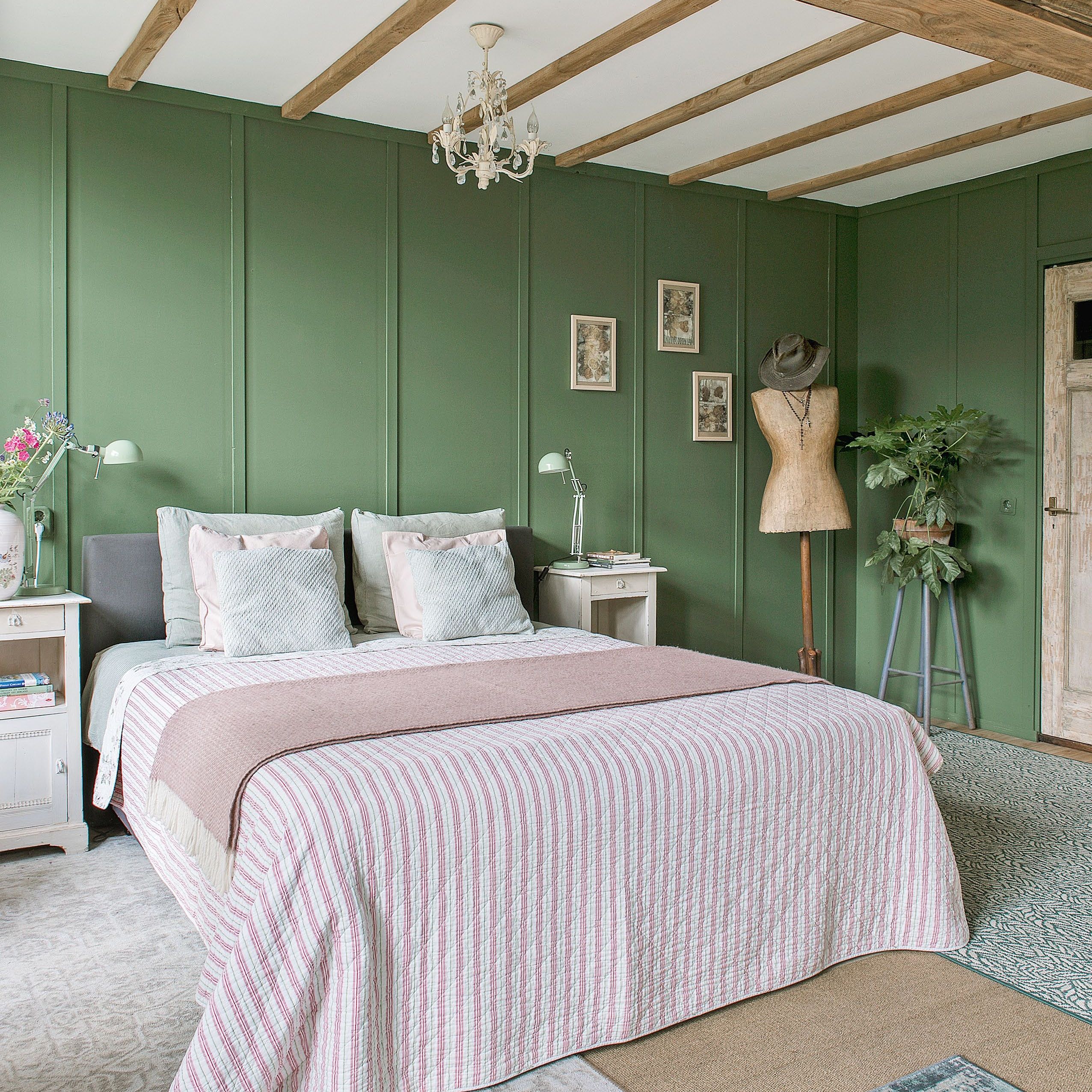 Bedroom with dark green painted wall panelling, ceiling beams and pink striped bedspread