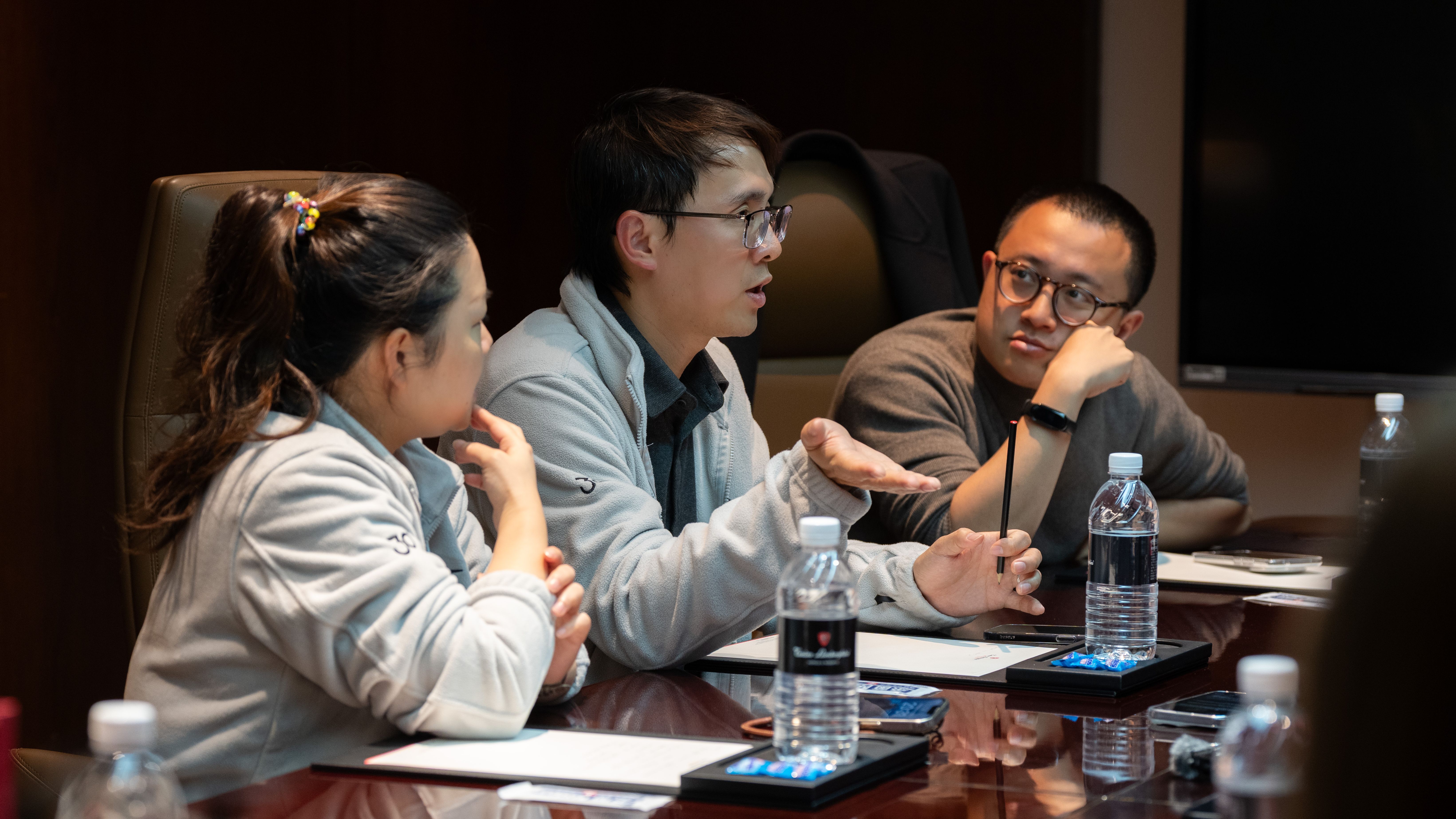 Three Lexar representatives engage in an active discussion around a dark wood conference table with water bottles and notebooks during a press conference.