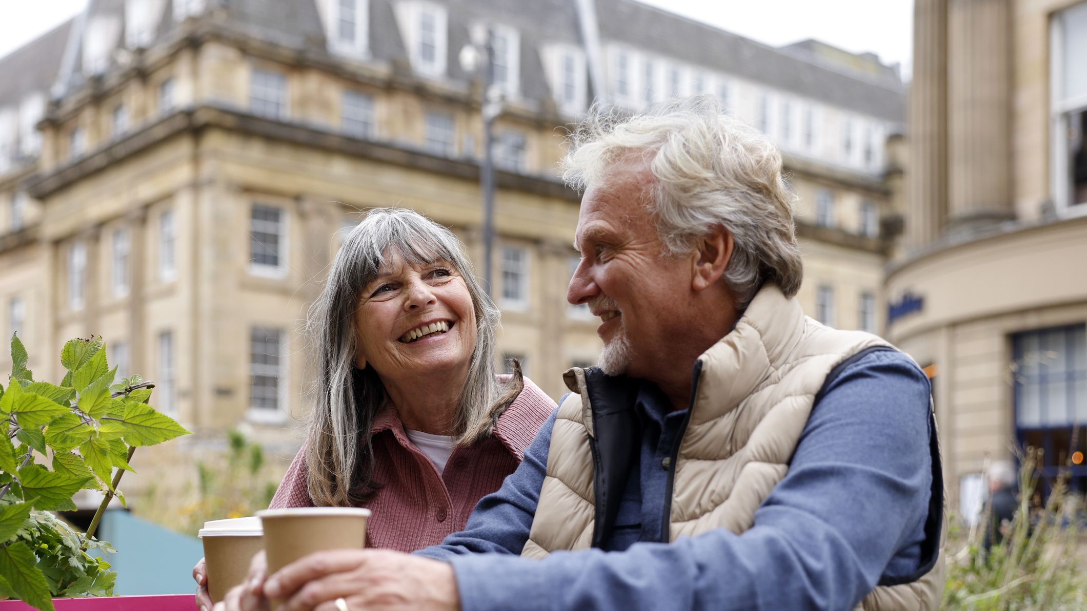 A happy senior couple enjoy a moment together while seated at an outdoor city caf&amp;eacute; during a city break. The scene captures companionship, relaxation and the pleasure of exploring a new destination together.