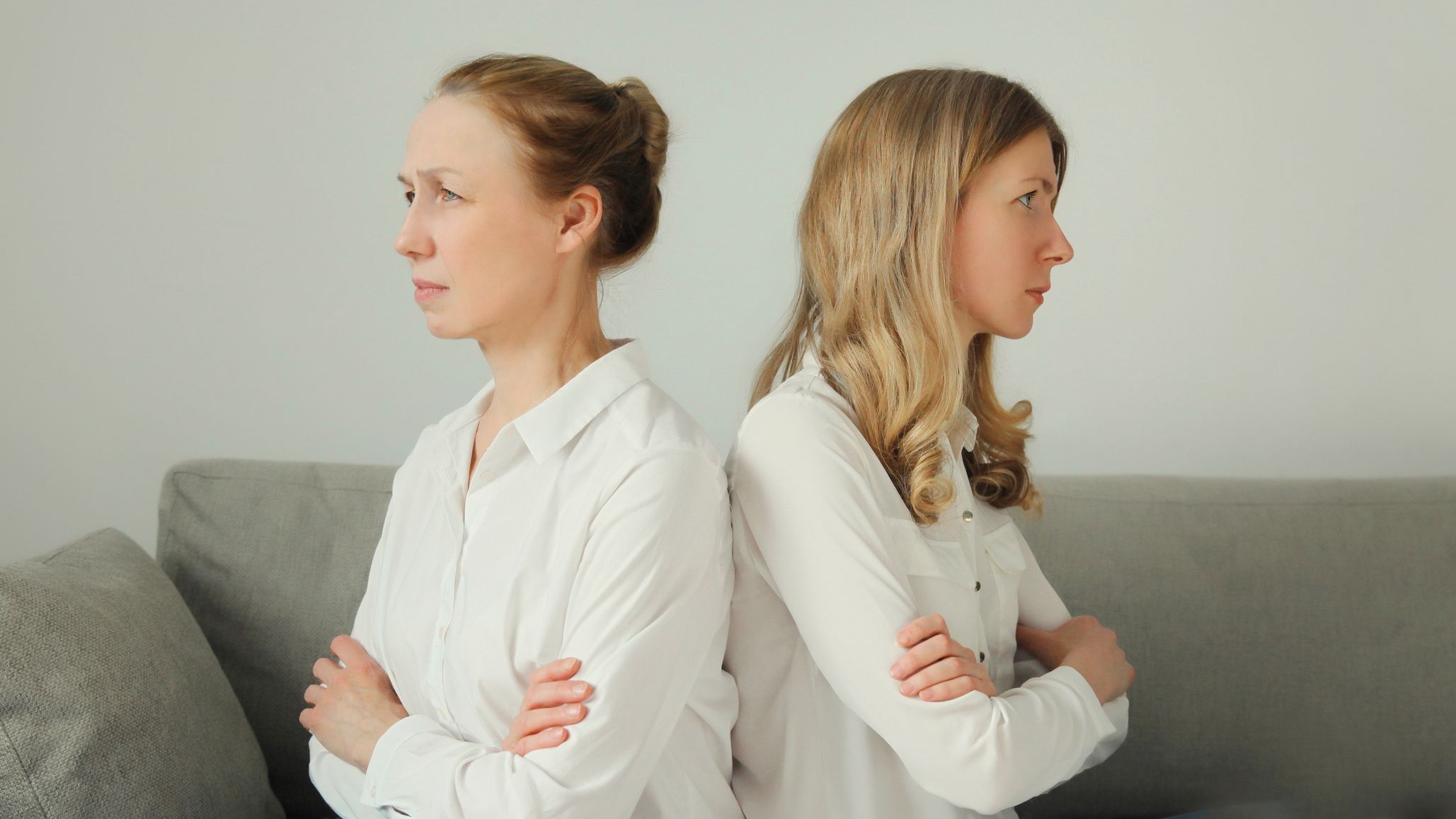 two sisters sit with their backs to each other arms folded
