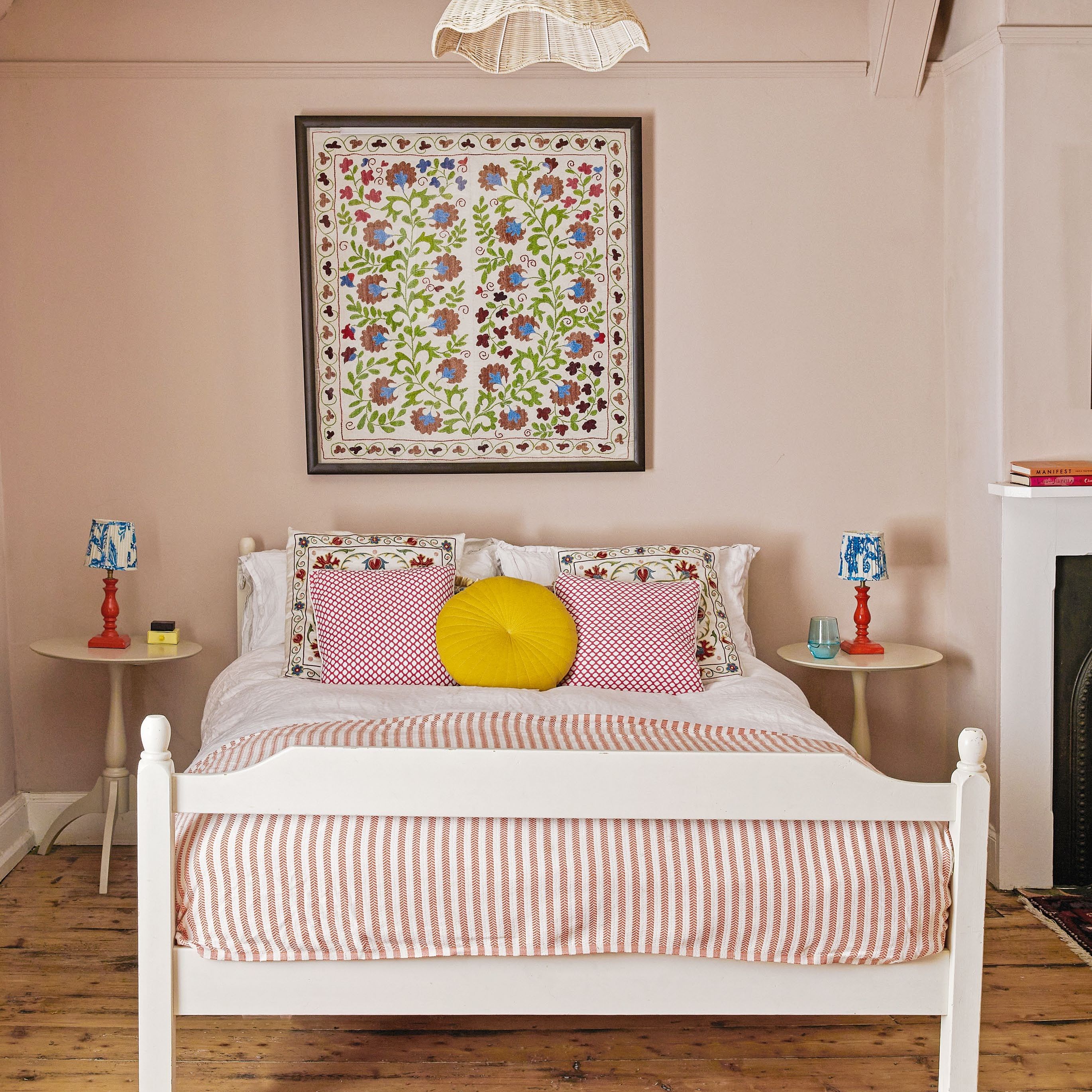 Pink bedroom with simple white painted wooden bed frame, striped throw and mixed scatter cushions
