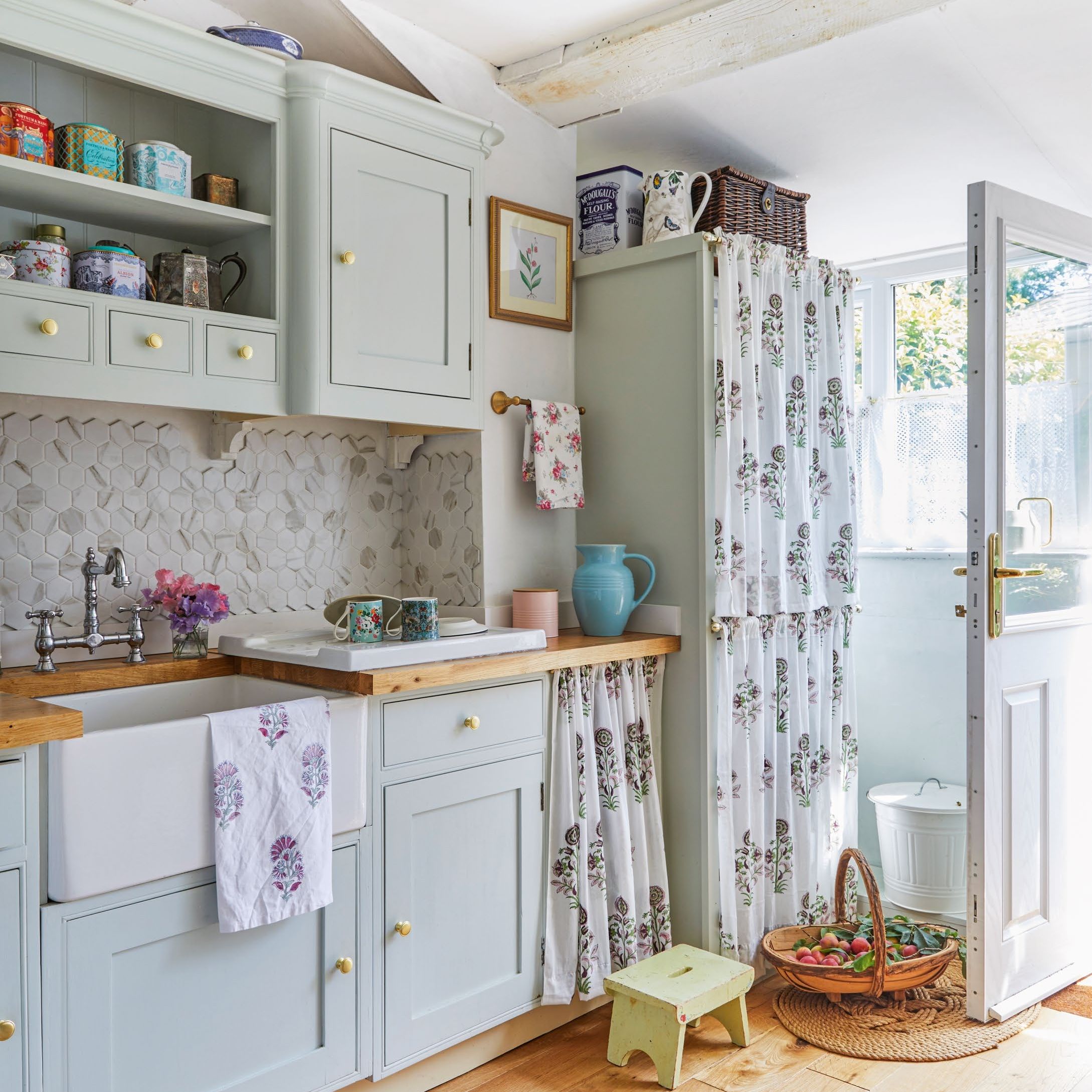 small cottage kitchen with butler sink, pale blue units, cupboard curtains and wooden worktops
