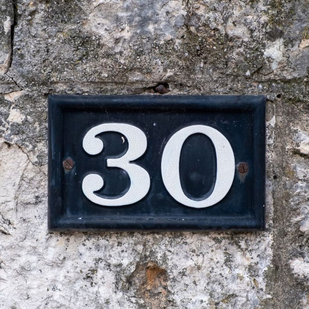 Street number 30. House address metal sign on stone wall.
