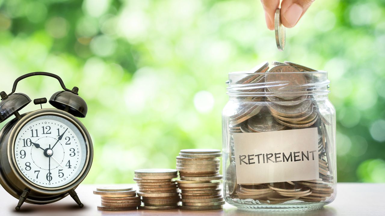 Hand putting Coins in glass jar with retro alarm clockfor time to money saving for retirement concept