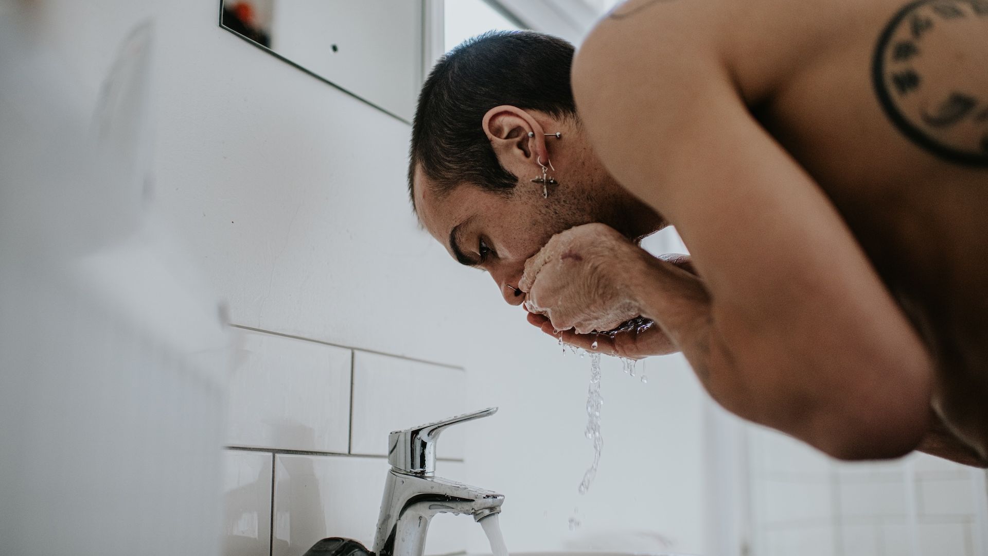 A man washes his face in a bathroom sink as the water flows from the faucet.