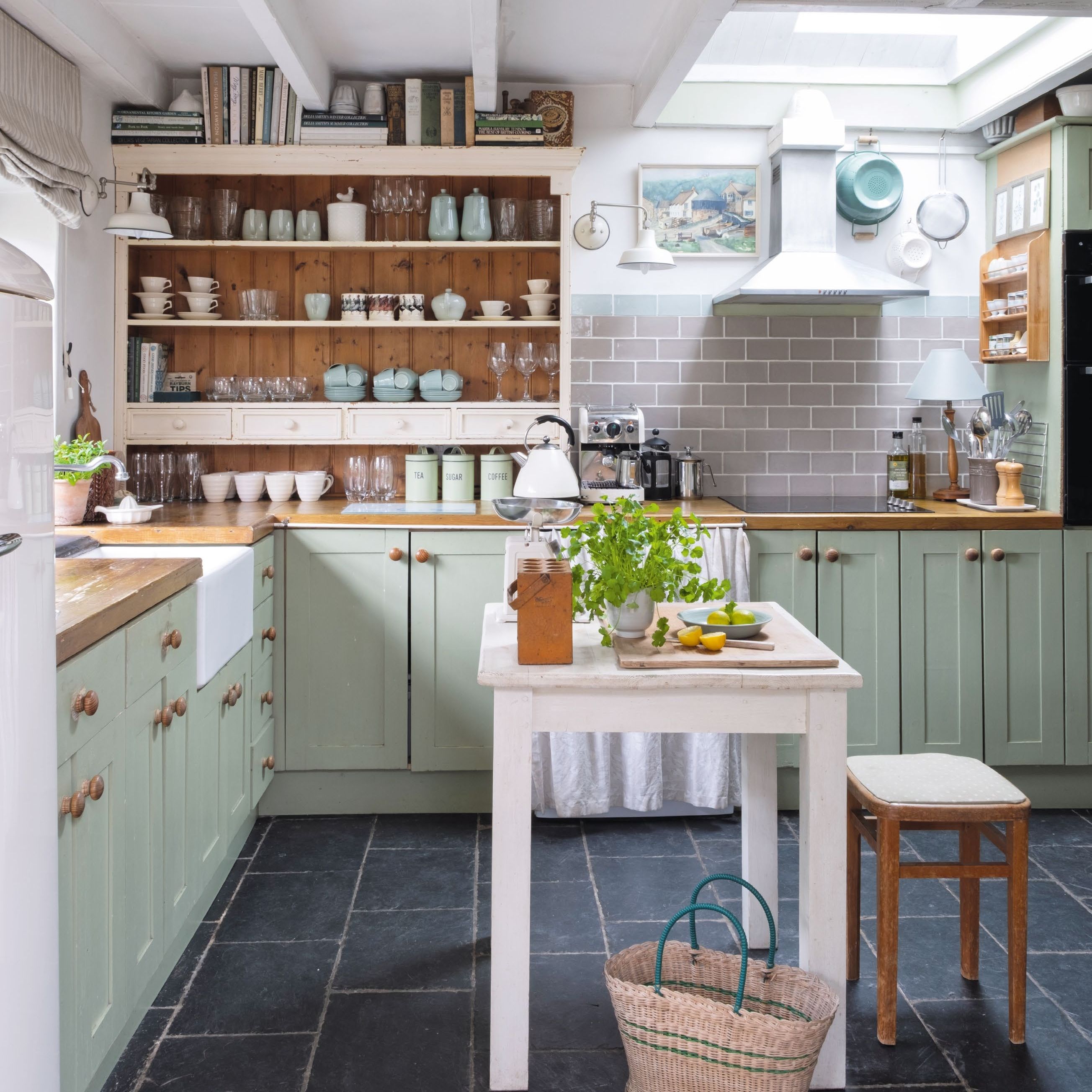Country kitchen with green units, open shelves and dark grey slate floor tiles