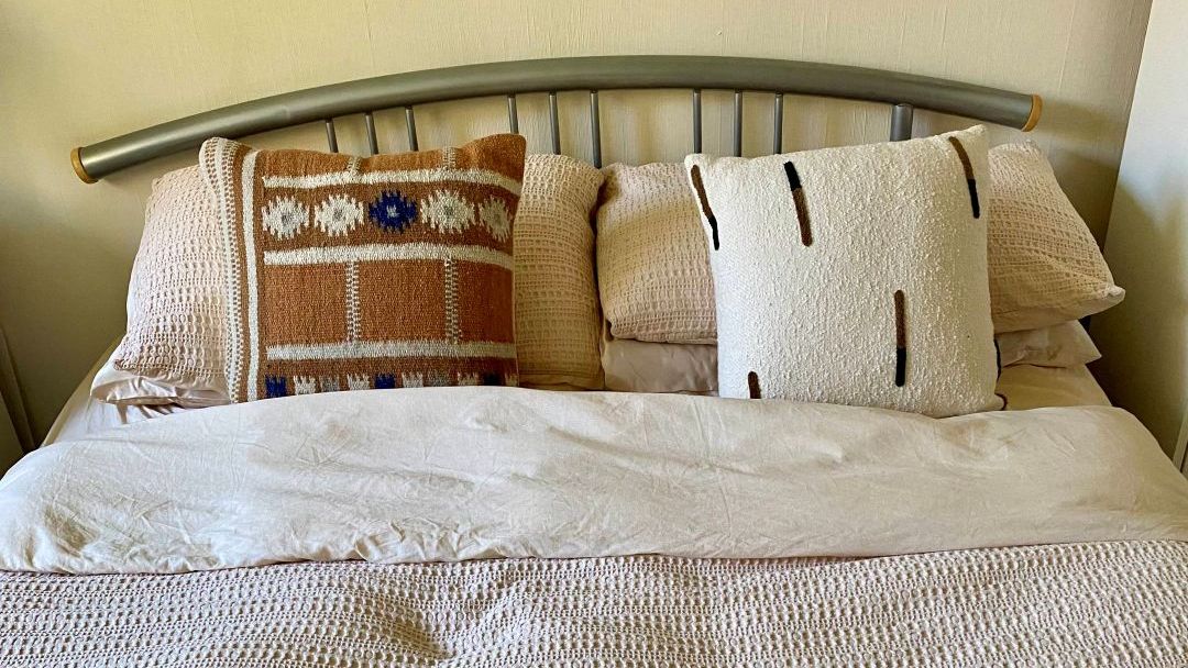 bed with neutral bedding, two cushions and a throw