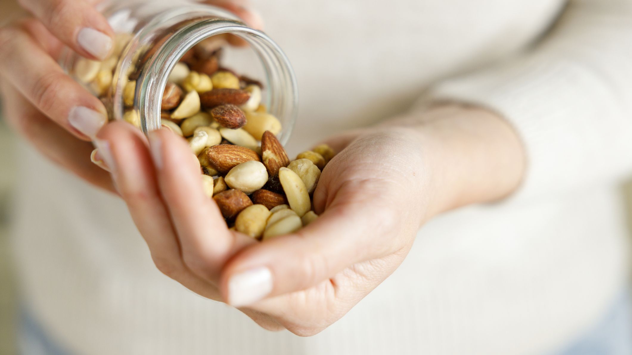 Nuts spilling from jar into woman&#039;s hand