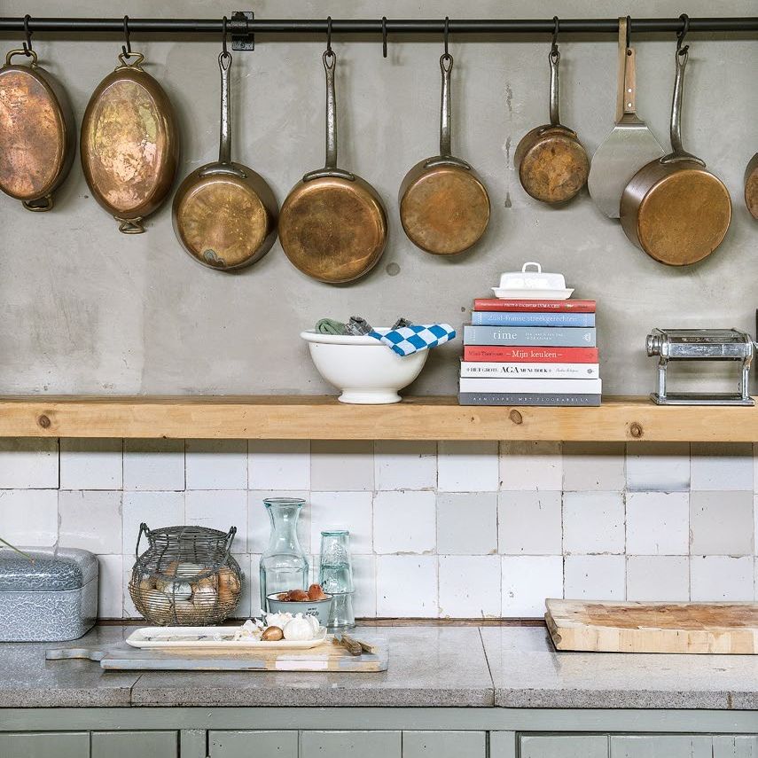 copper pans hanging from a rail in a kitchen with tiled splashback