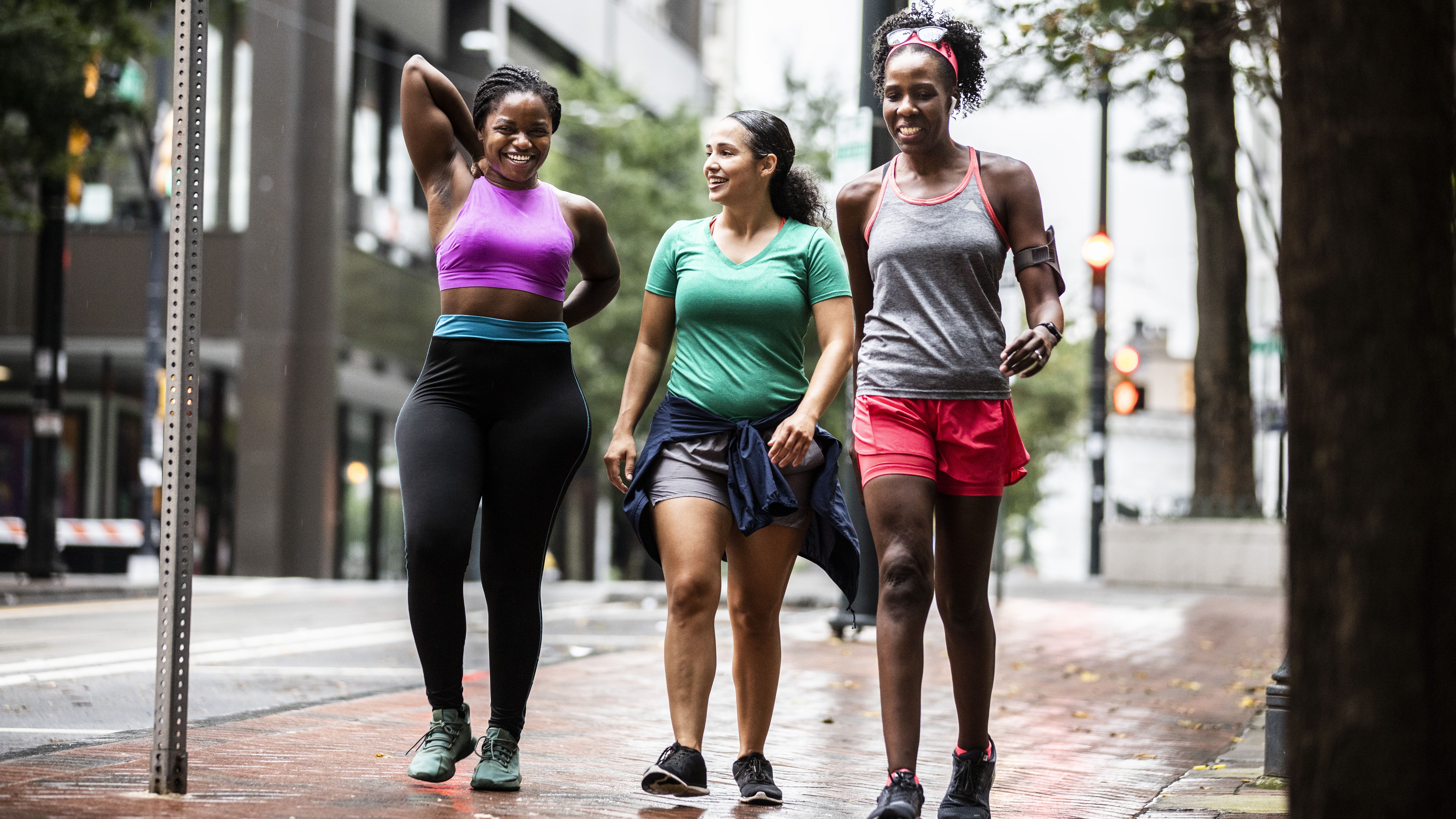 A group of three women walk together along the street smiling.