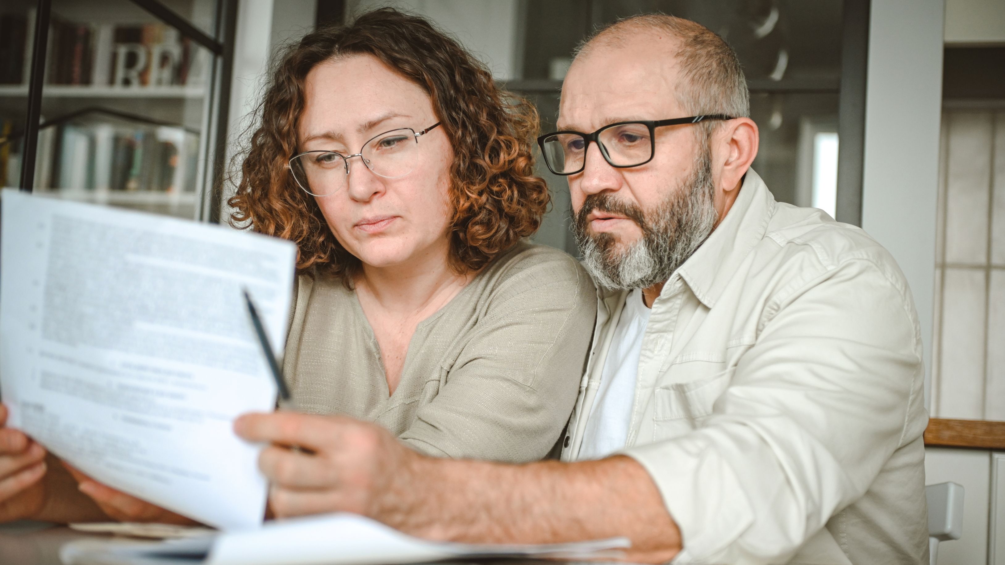 A mature couple reviews paperwork while sitting at their dining table.