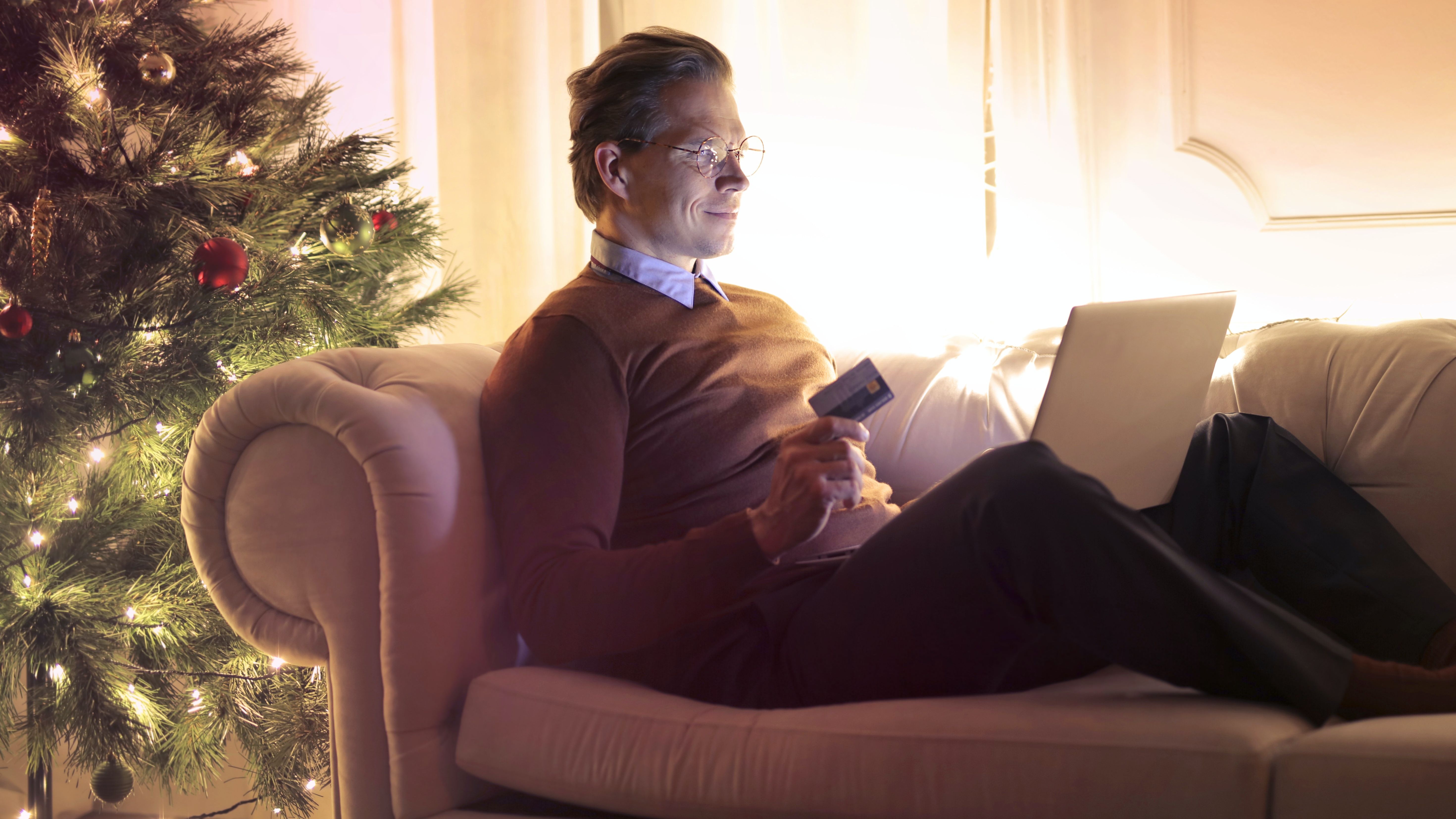 Man in Brown Long Sleeve Sweater and Black Pants Sitting on Brown Sofa Chair Using Laptop