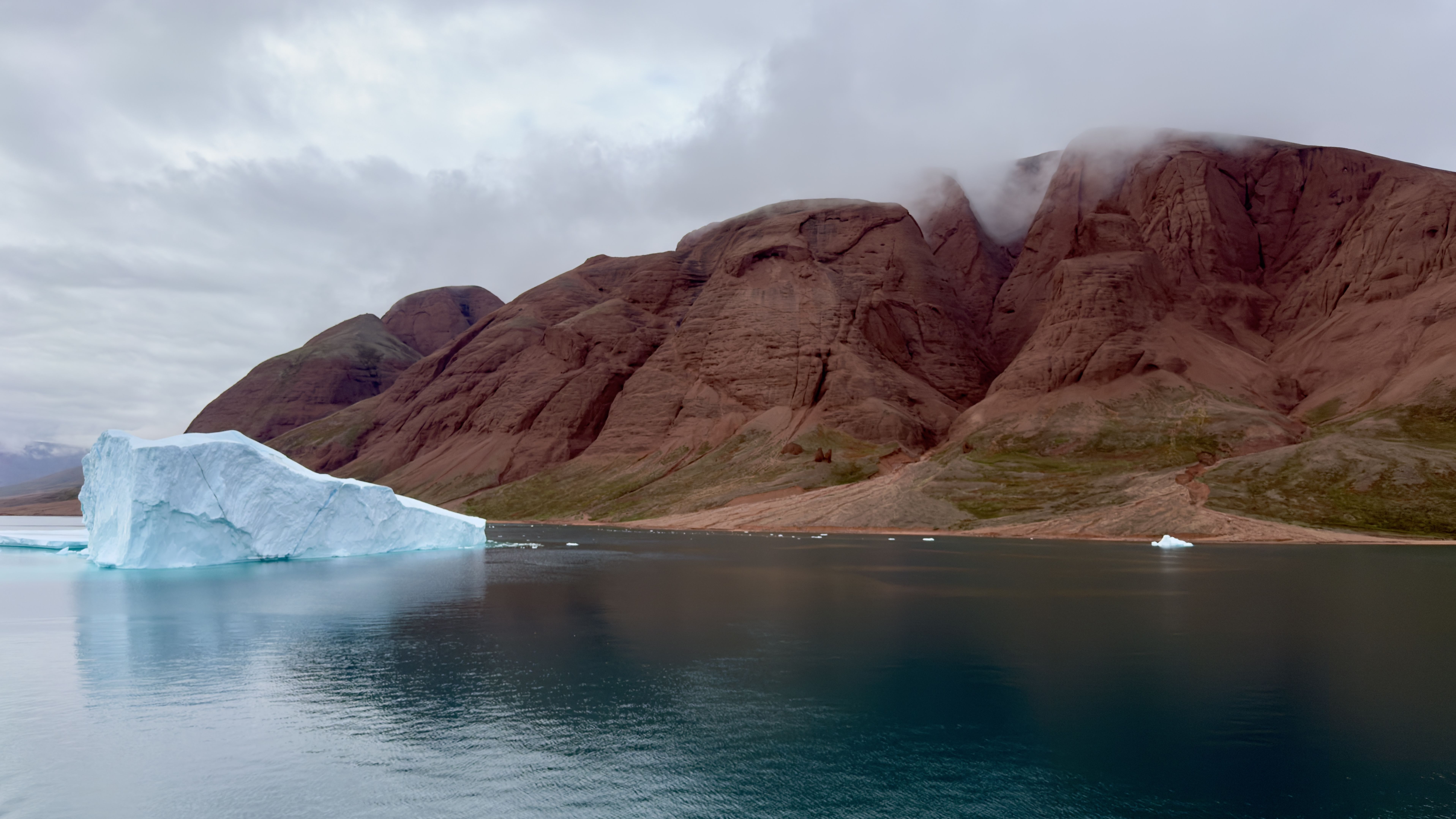 I sailed to Greenland for a total solar eclipse — what I saw left me speechless 9 MyCelestialApp rusty red rocks, blue water in the foreground a a large iceberg make for striking contrast