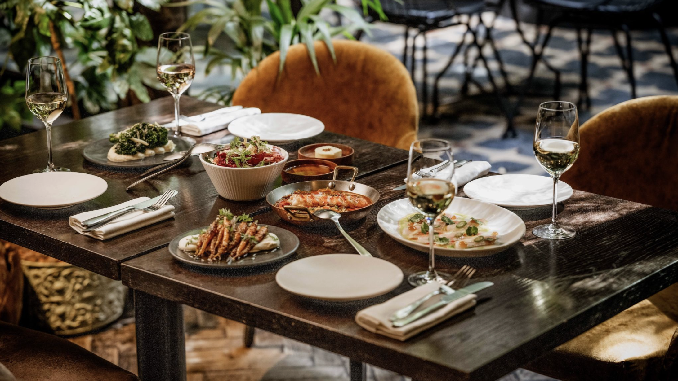 an image of a table of four at Yopo with different plates from the menu with four glasses of white wine at each place setting