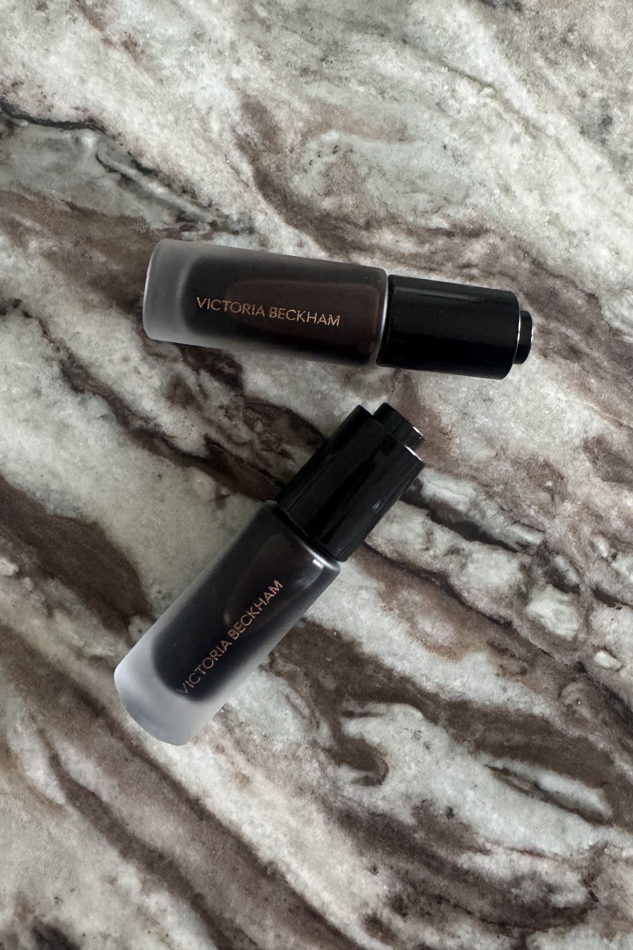 The Victoria Beckham Beauty Colour Wash Bronze Tint in Tanline and Heatwave side by side on a marble table