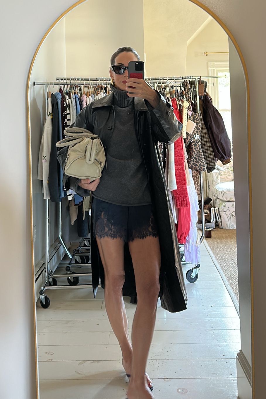 Larissa Mills in blue lace shorts, gray sweater, and black leather trench coat