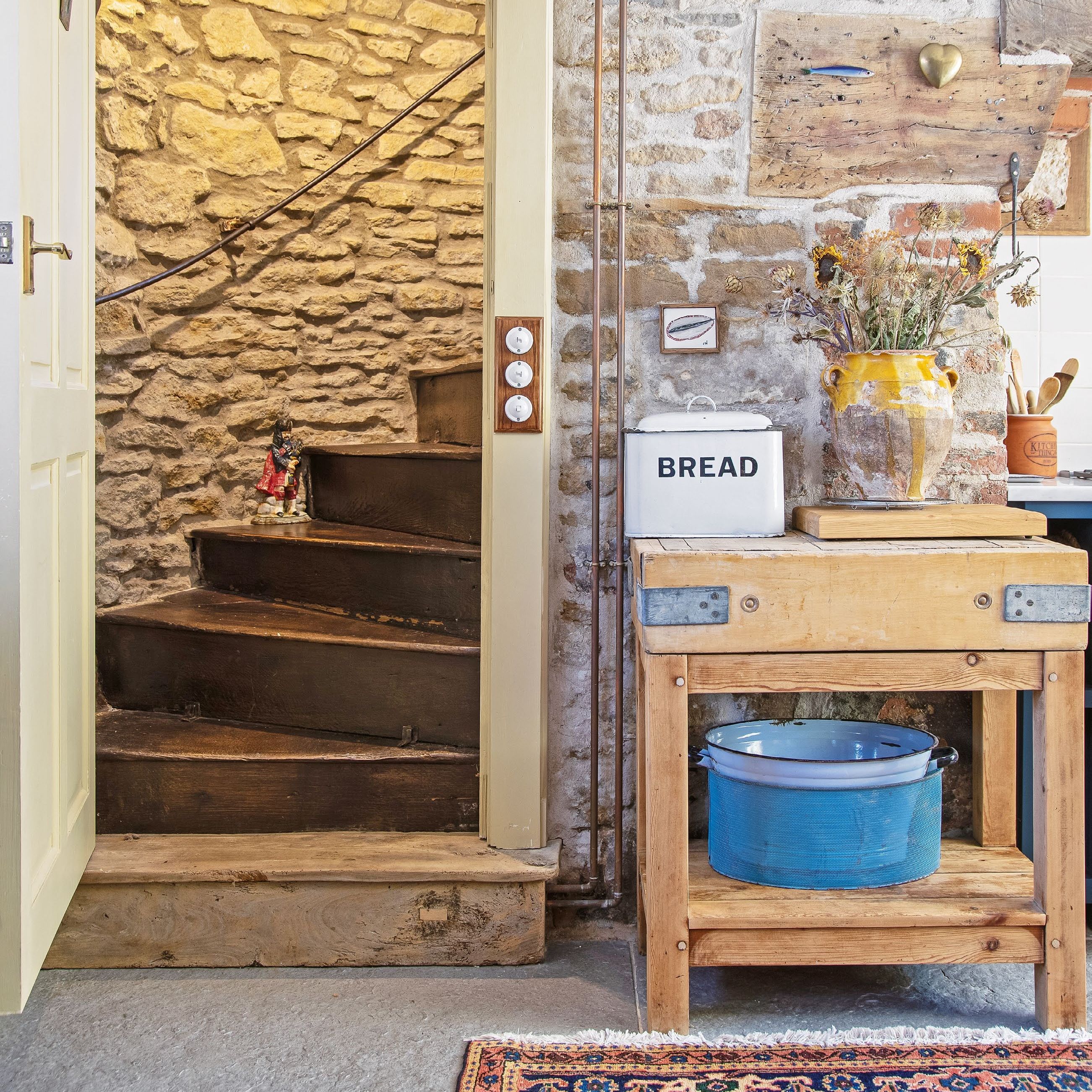 Corner of country cottage kitchen with exposed stone wall and door leading to curved wooden staircase