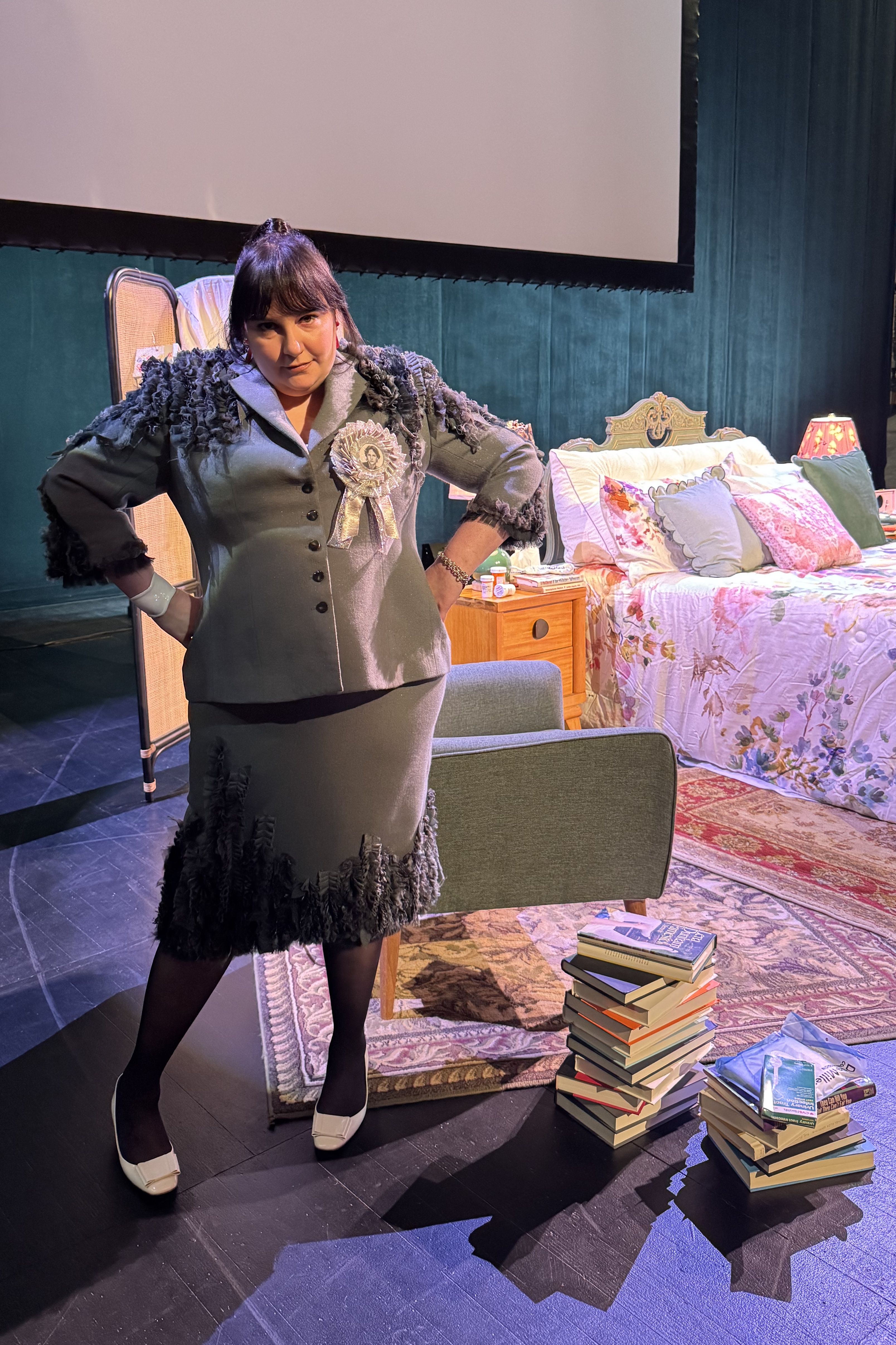 Lena Dunham during her Famesick book tour wearing a gray skirt suit and white prize ribbon pin