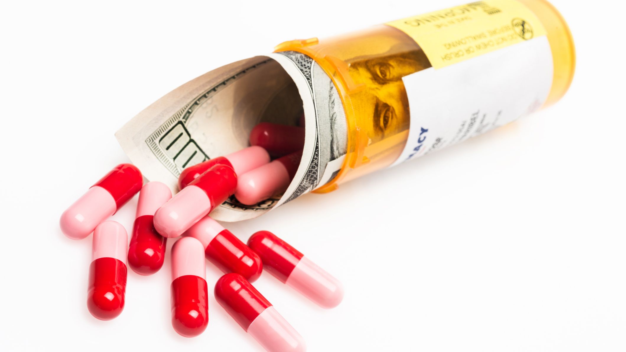 rolled 100 dollar bill inside a prescription drug container and pills on white background
