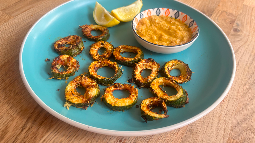 Crisped rings of zucchini, a dip in a small blue and lemon wedges on a blue plate on a wooden table