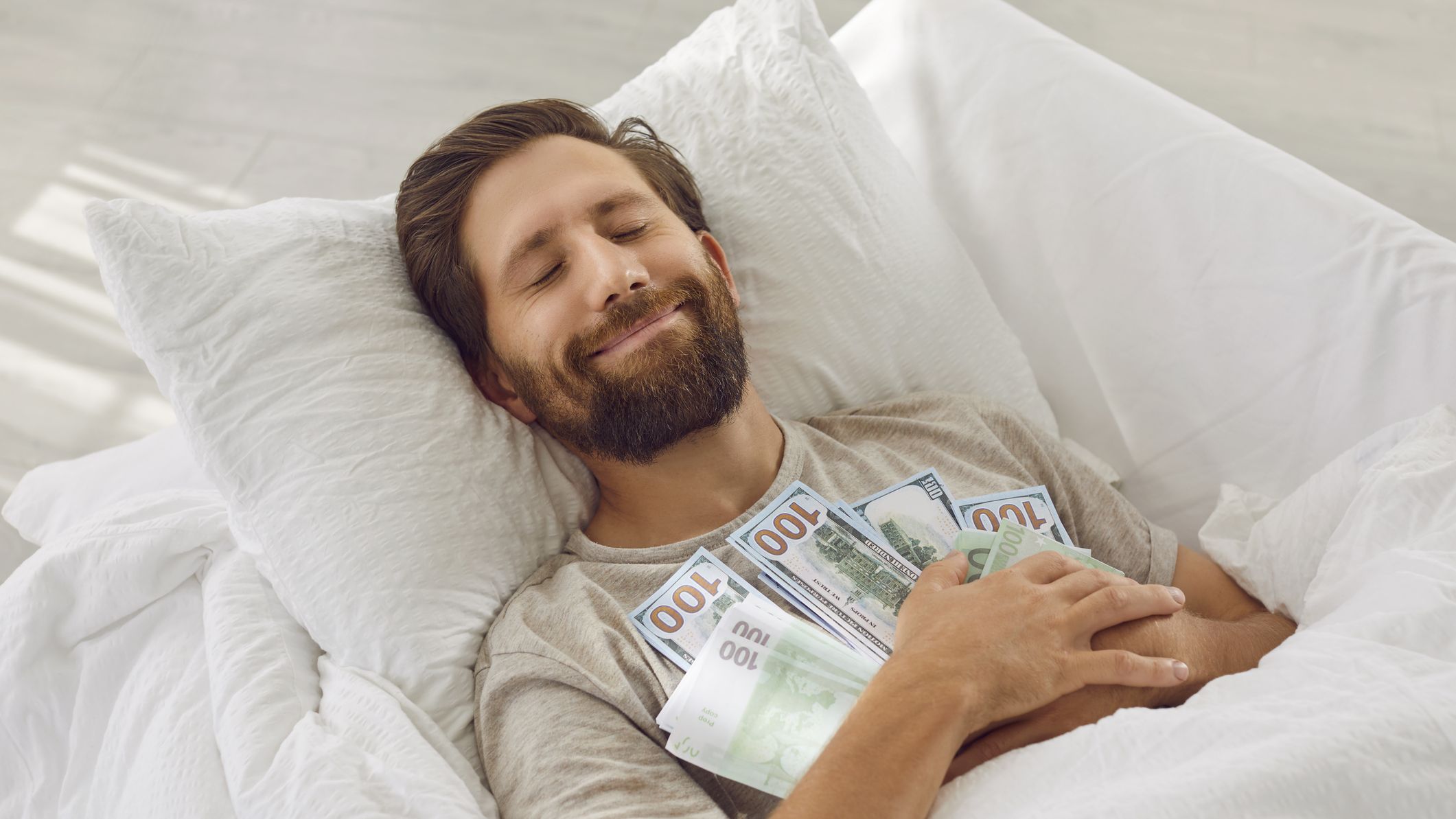 Man sleeping in a bed holding a lot of money