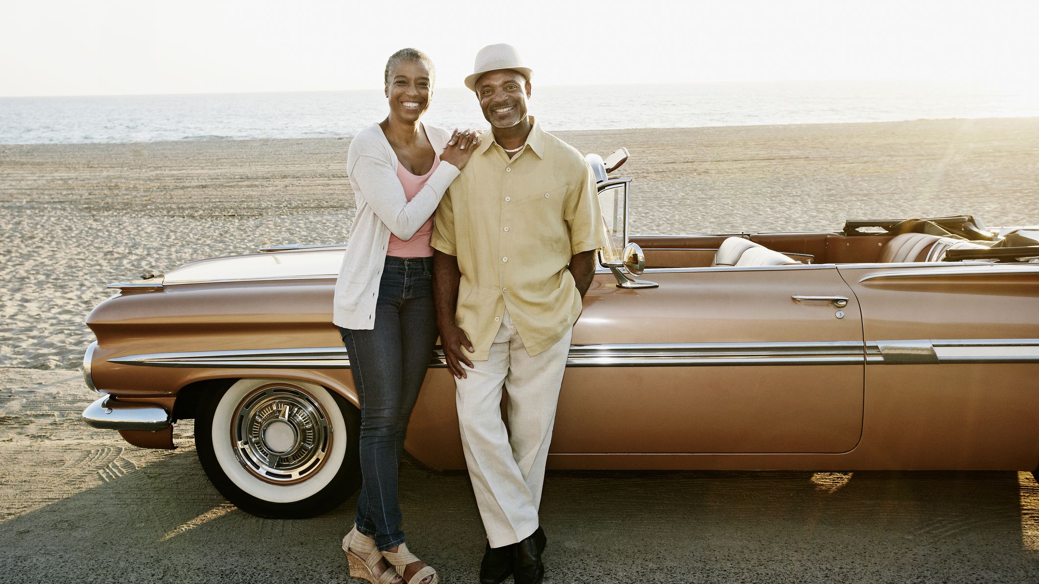 A retired couple poses in front of their classic convertible car.
