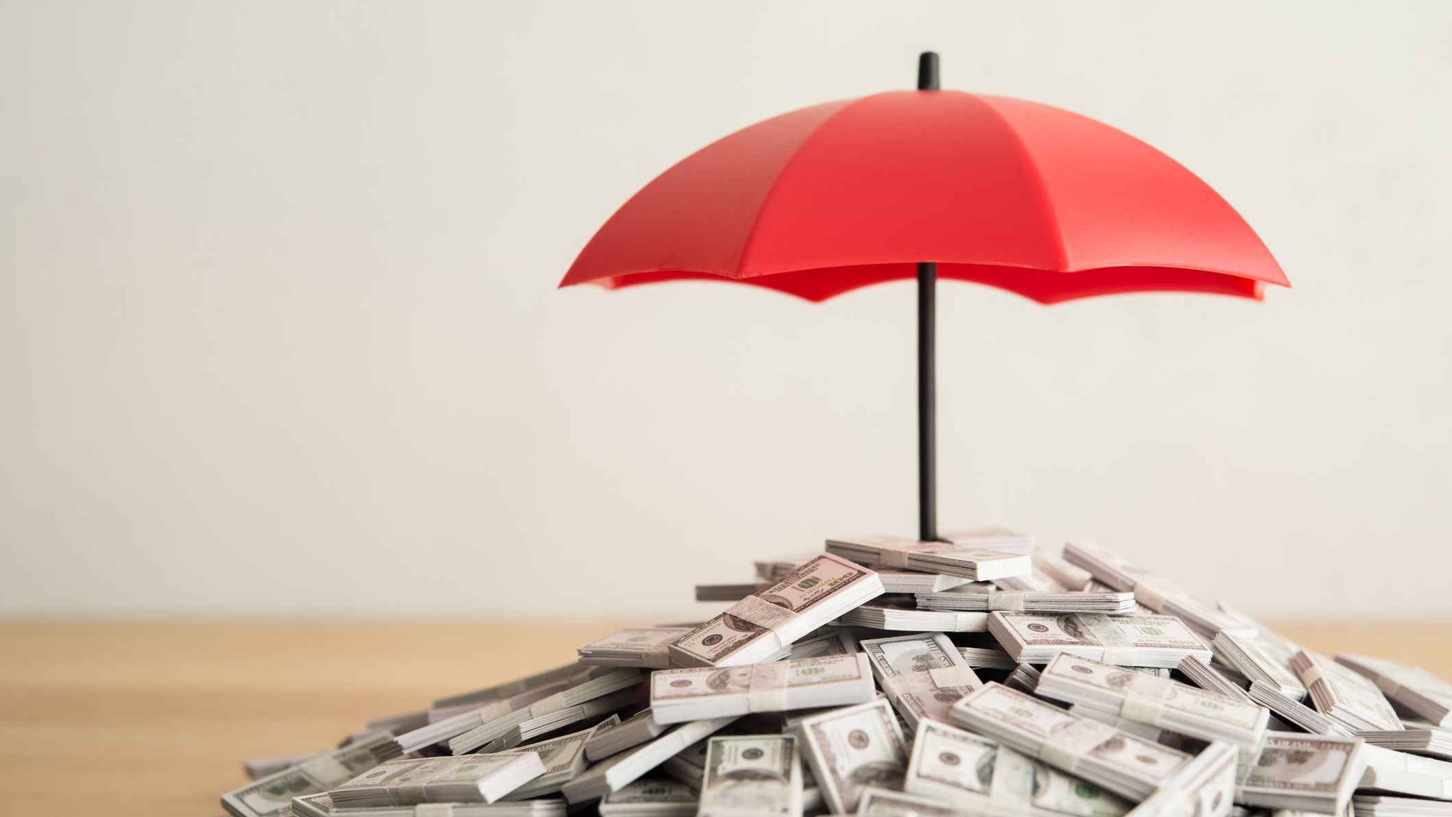 a stack of cash tucked under an umbrella indicating financial protection