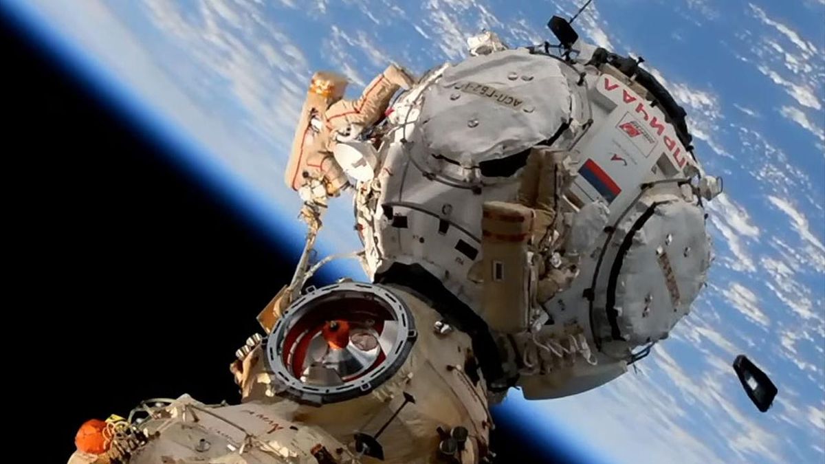 prichal module of international space station with cosmonauts doing a spacewalk. a container floats away at lower right