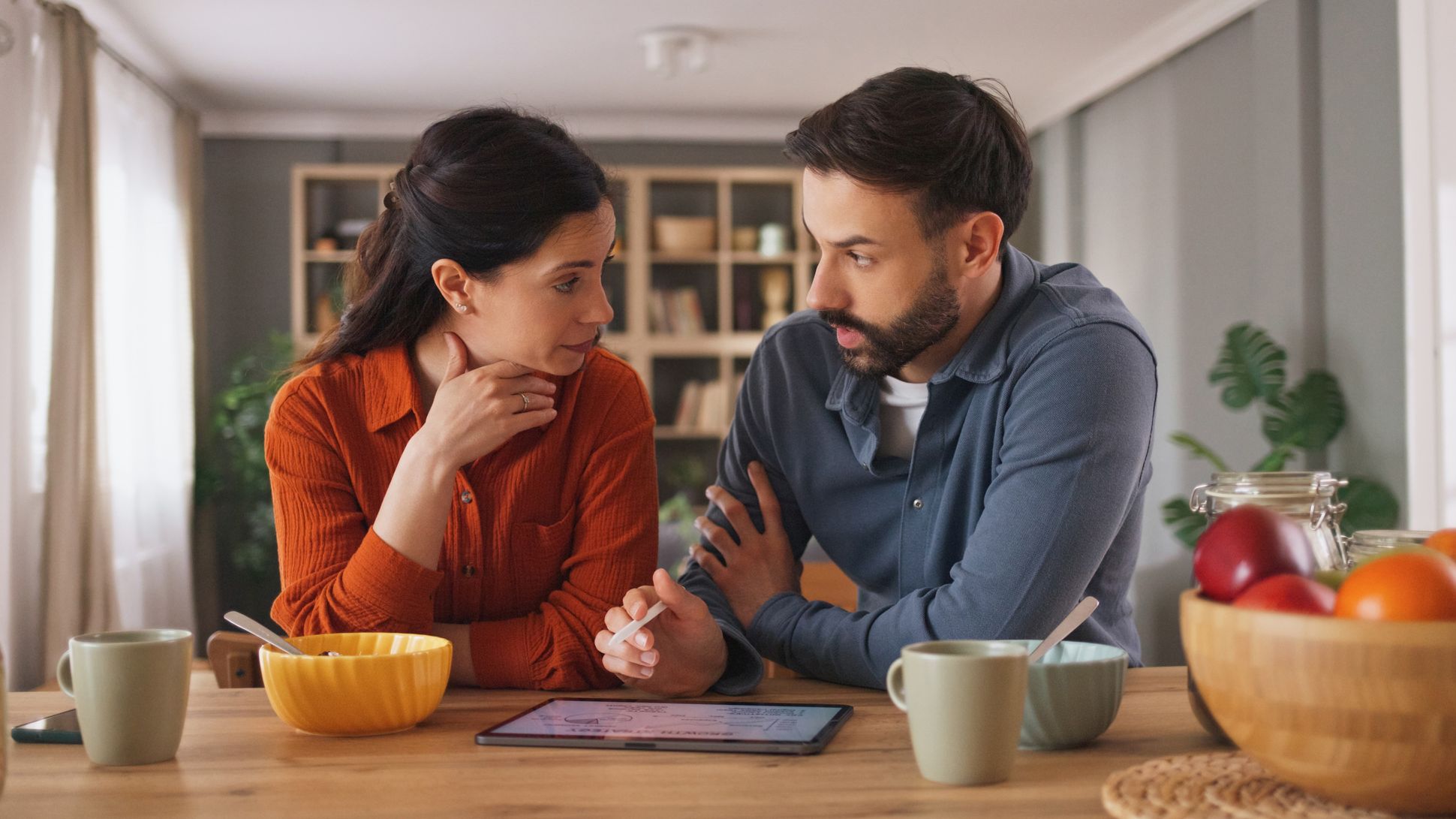 Couple discussing finances over breakfast at home using digital tablet