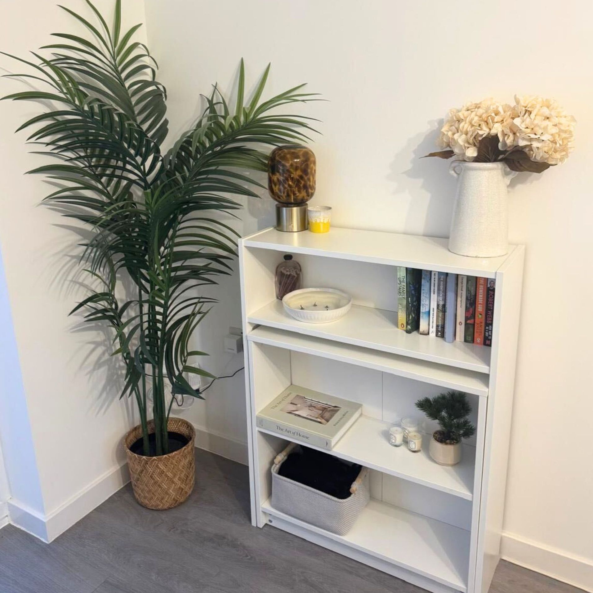 A decorated IKEA Billy bookcase against a white wall with a tall houseplant next to it