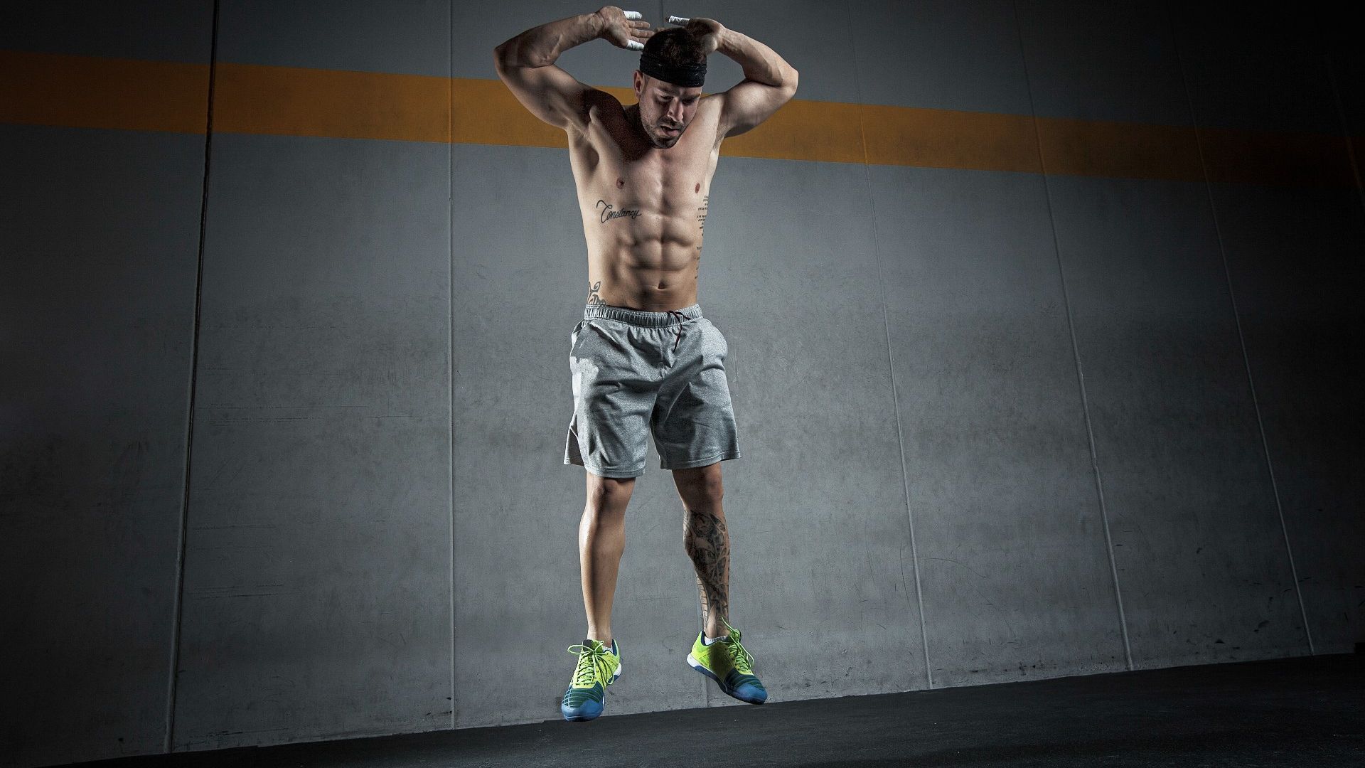 Man performing a burpee against a grey backdrop jumping into the air with his hands behind his head