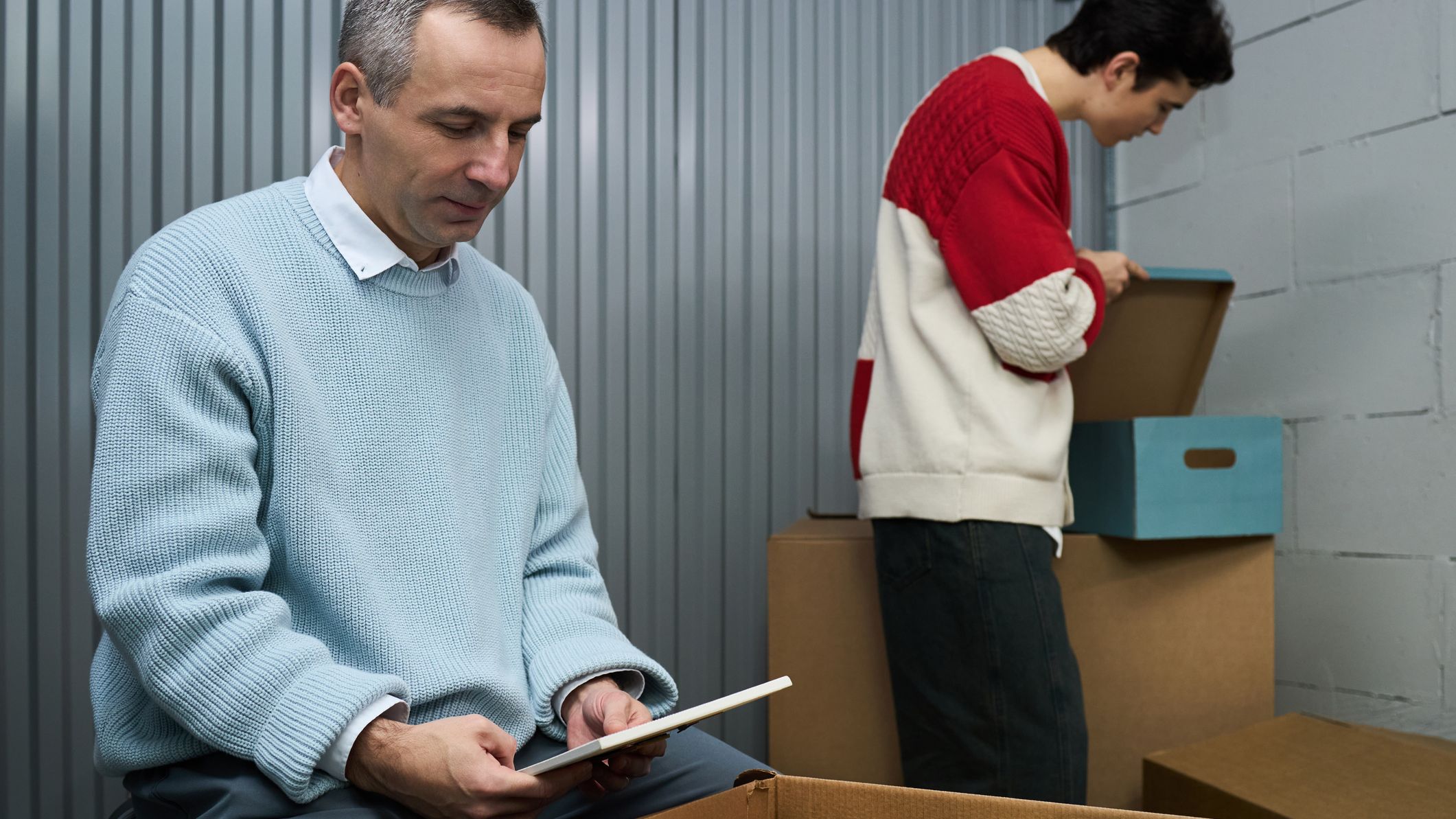 Middle Aged Man Packing Boxes While Young Adult Man Organizing Items