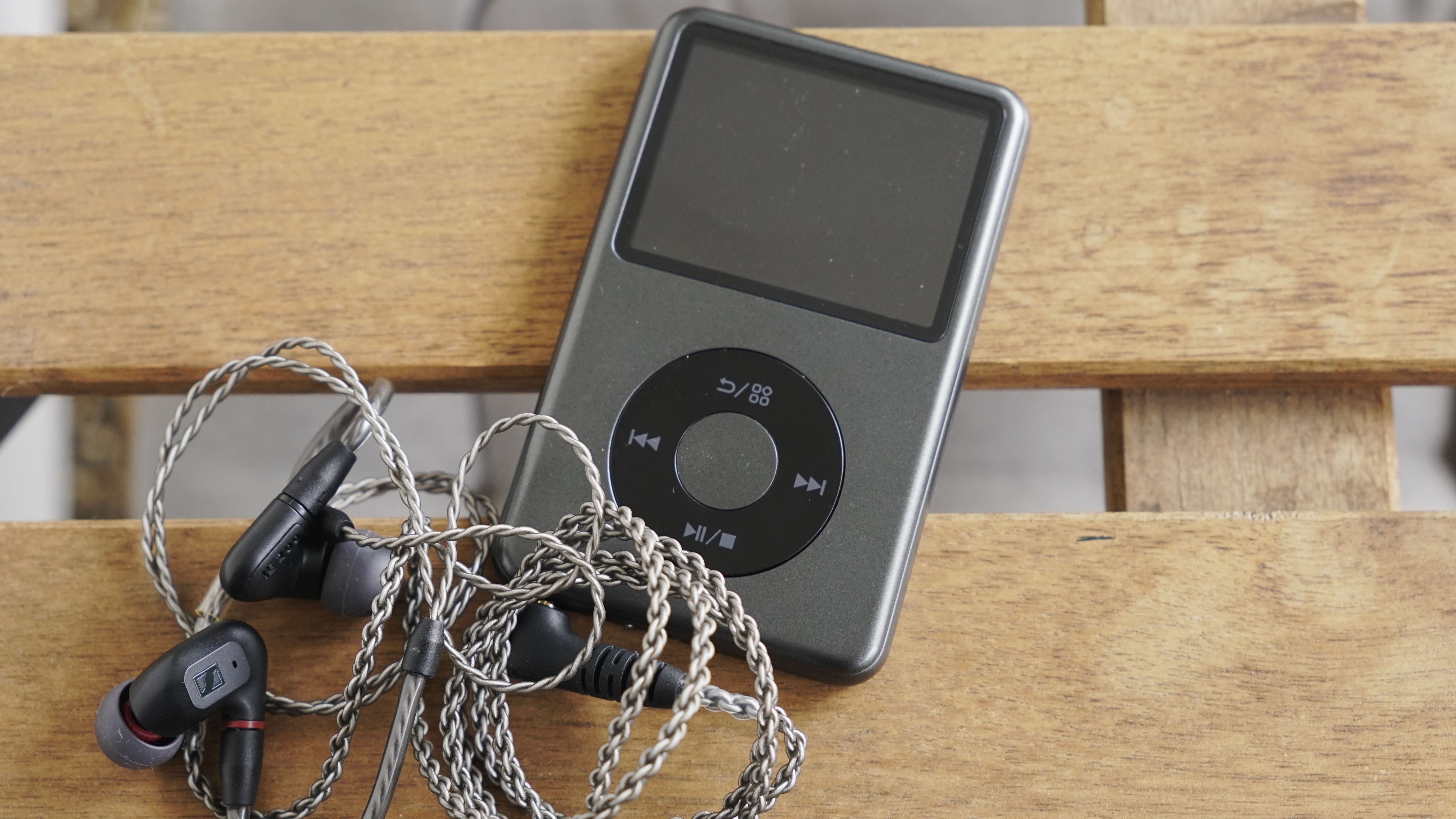 Innioasis Y1 player held in a man's hand, showing the dial and screen, with a wooden table in the background