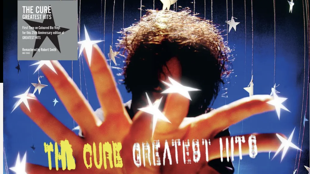 A screen-grab from The Cure's Greatest Hits album, showing Roberth Smith putting his hands up to the camera to obscure his face, with white stars on his fingers and a blue background behind him