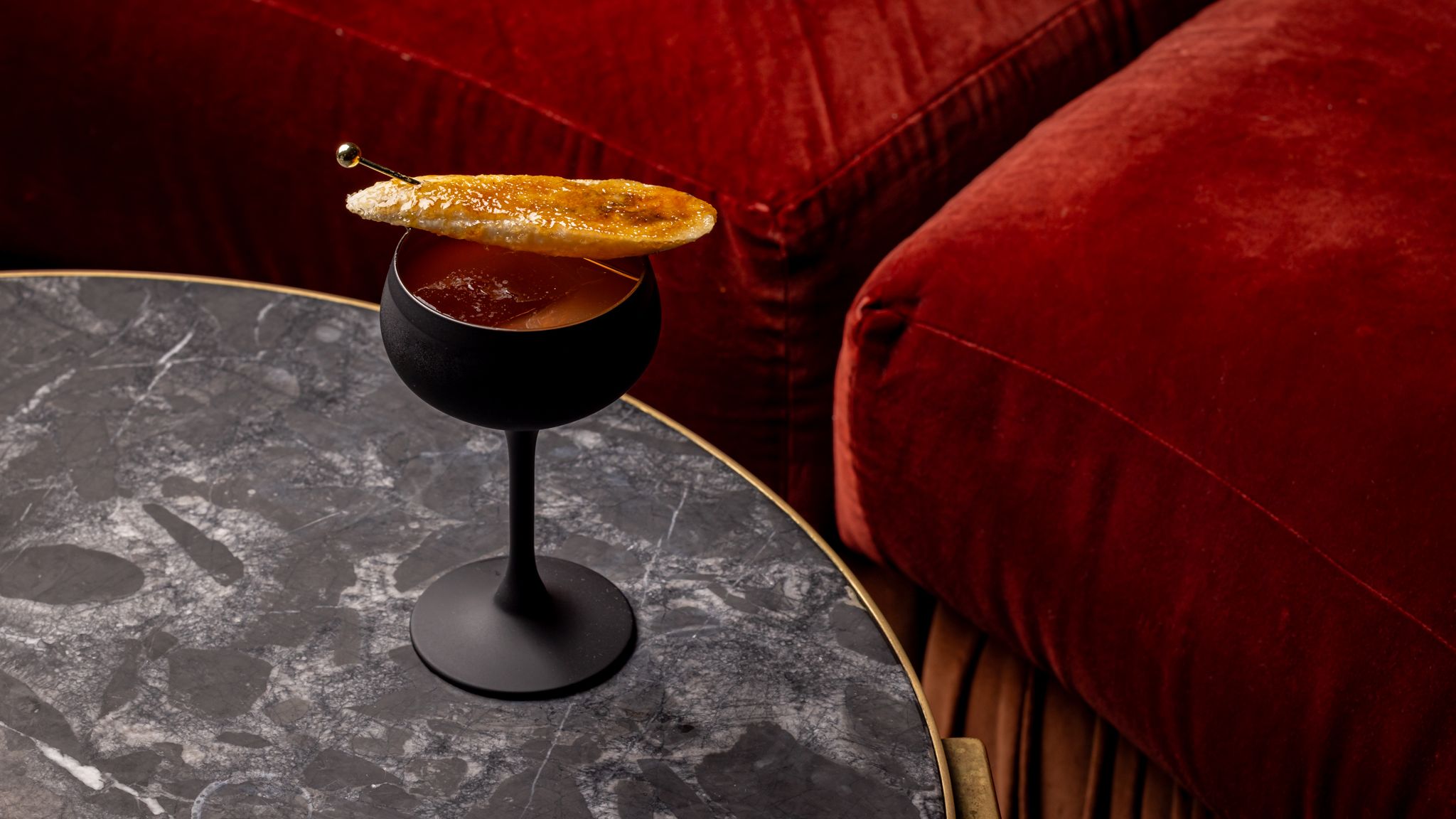 an image of the Black Hole cocktail at Fitzs' Bar in London on a round marble table against red velvet sofa seats