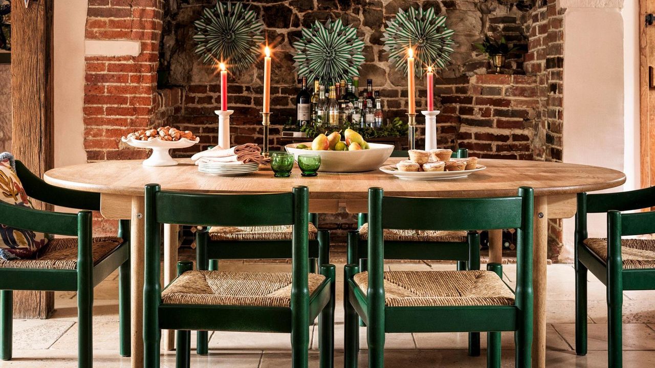 A cottage kitchen dining area with a wooden oval table, vintage chairs painted green, and an old fireplace converted into a home bar