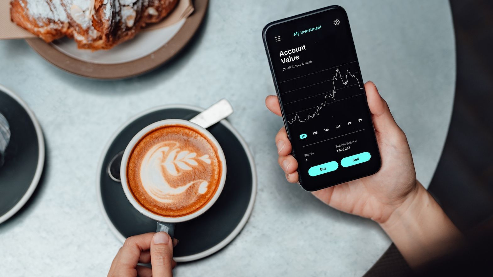 High angle view of a young woman checking the stock market on smartphone, having breakfast at coffee shop. Business on the go concept.