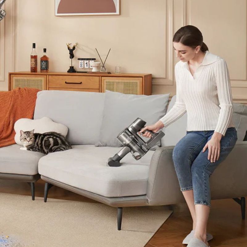 Three people using the Dreame R20 cordless vacuum in different configurations, vacuuming the rug, sofa, and picture fram in a brown living room with warm, neutral colors.