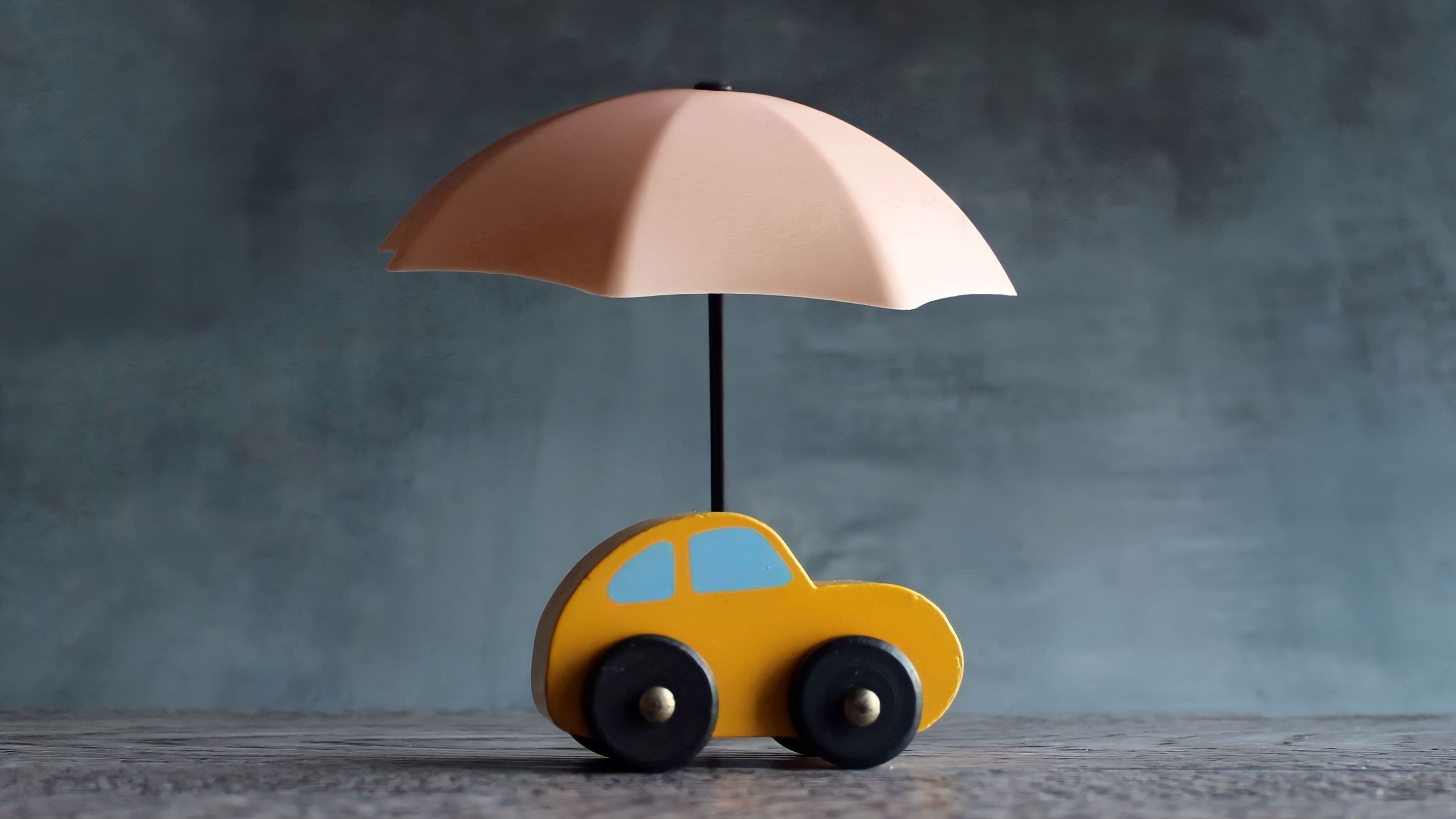 A toy car with an umbrella over it, indicating car insurance.