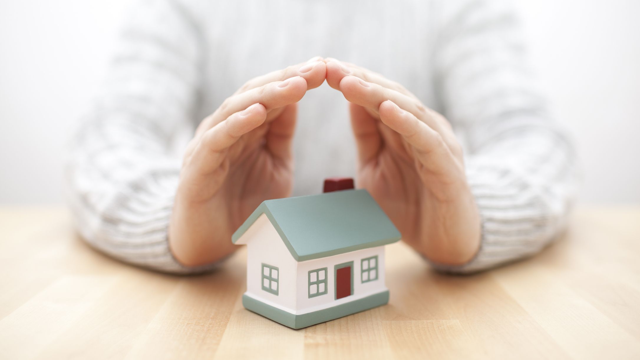 A person's hands covering a model of a home.