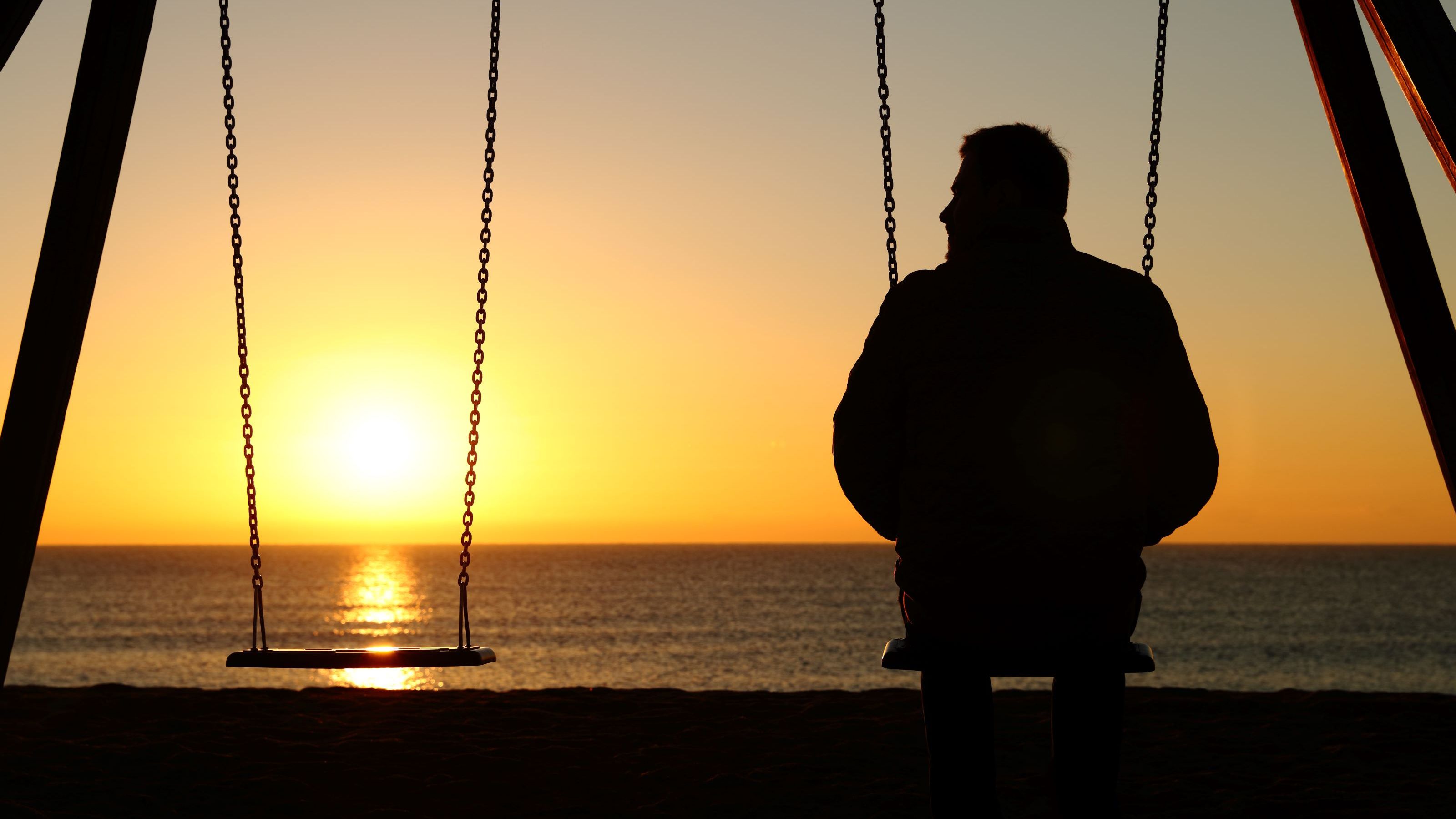 A man sits alone on a swing.