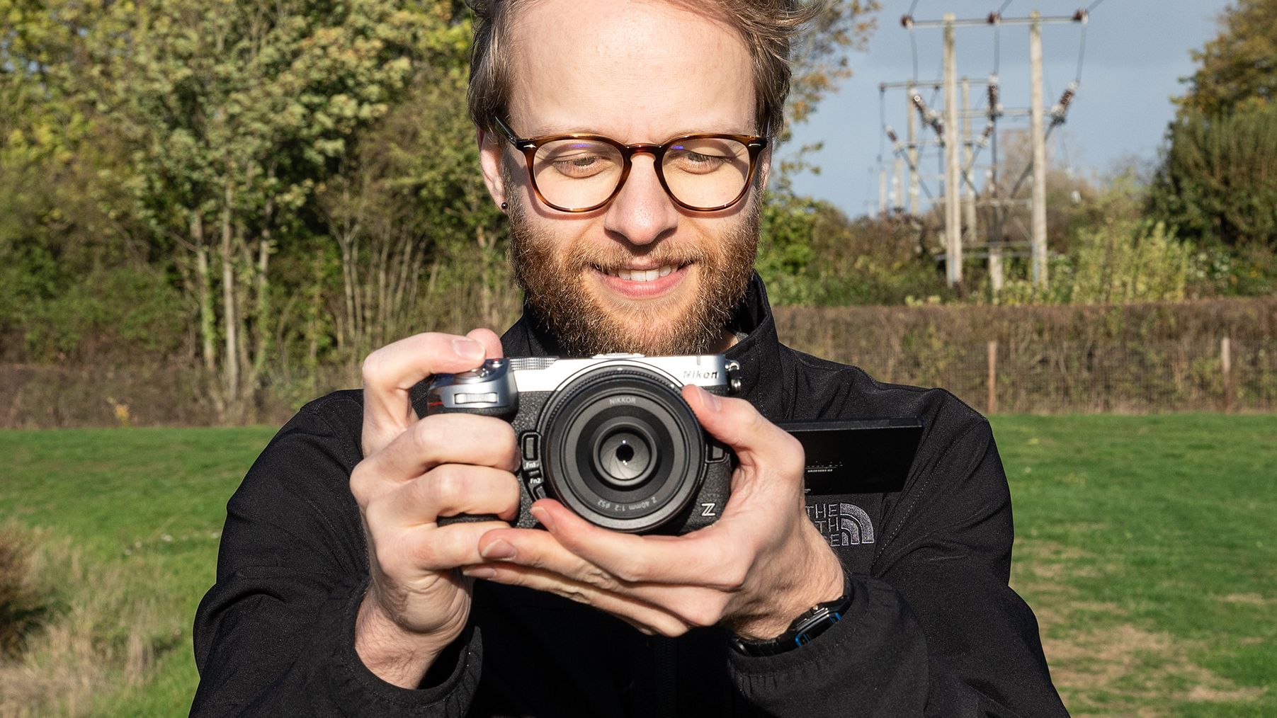 Mike Harris wearing a black jacket holding the Nikon Z5IIC on a green background